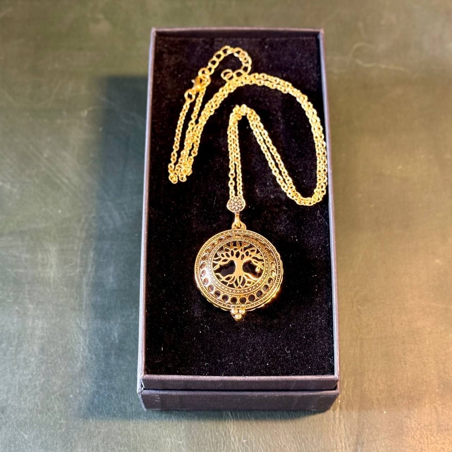 A gold-colored necklace with a pendant in the shape of a tree, displayed in a black jewelry box.