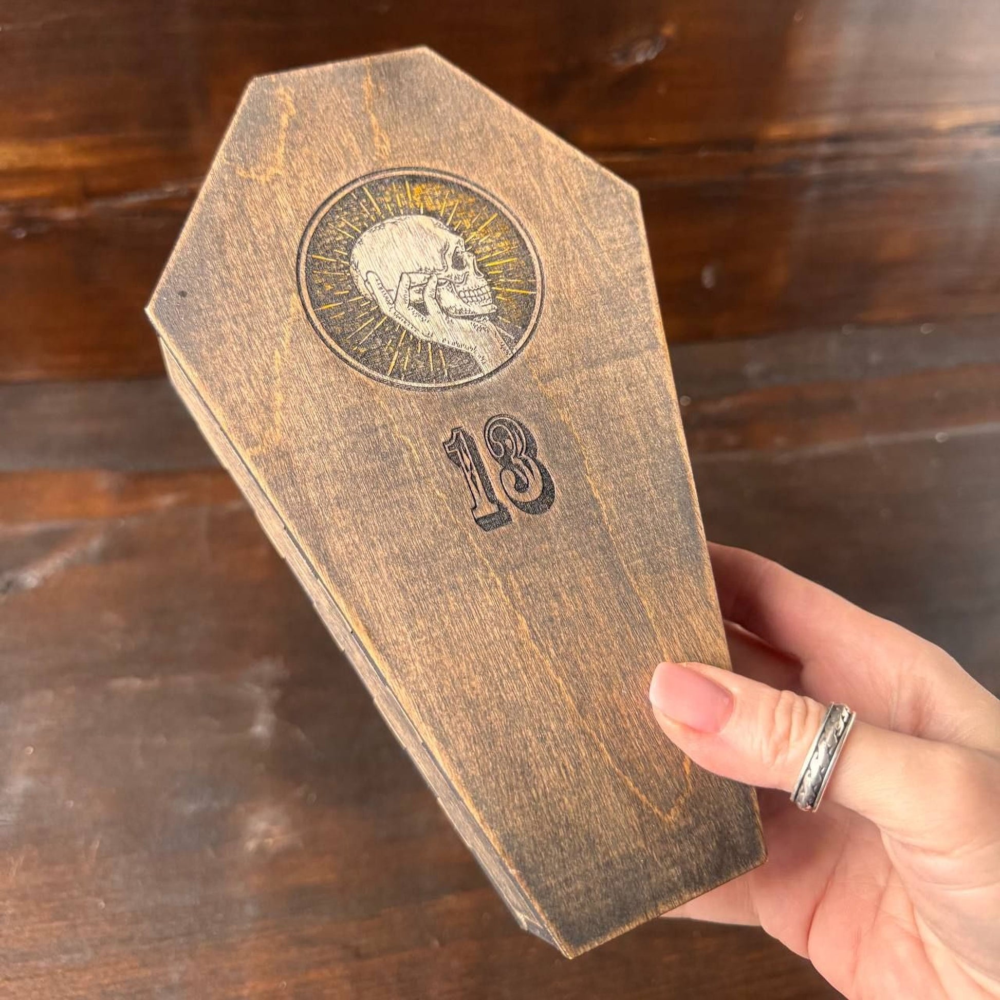 A hand holding a wooden box with a skull design and the number 18 printed on it.