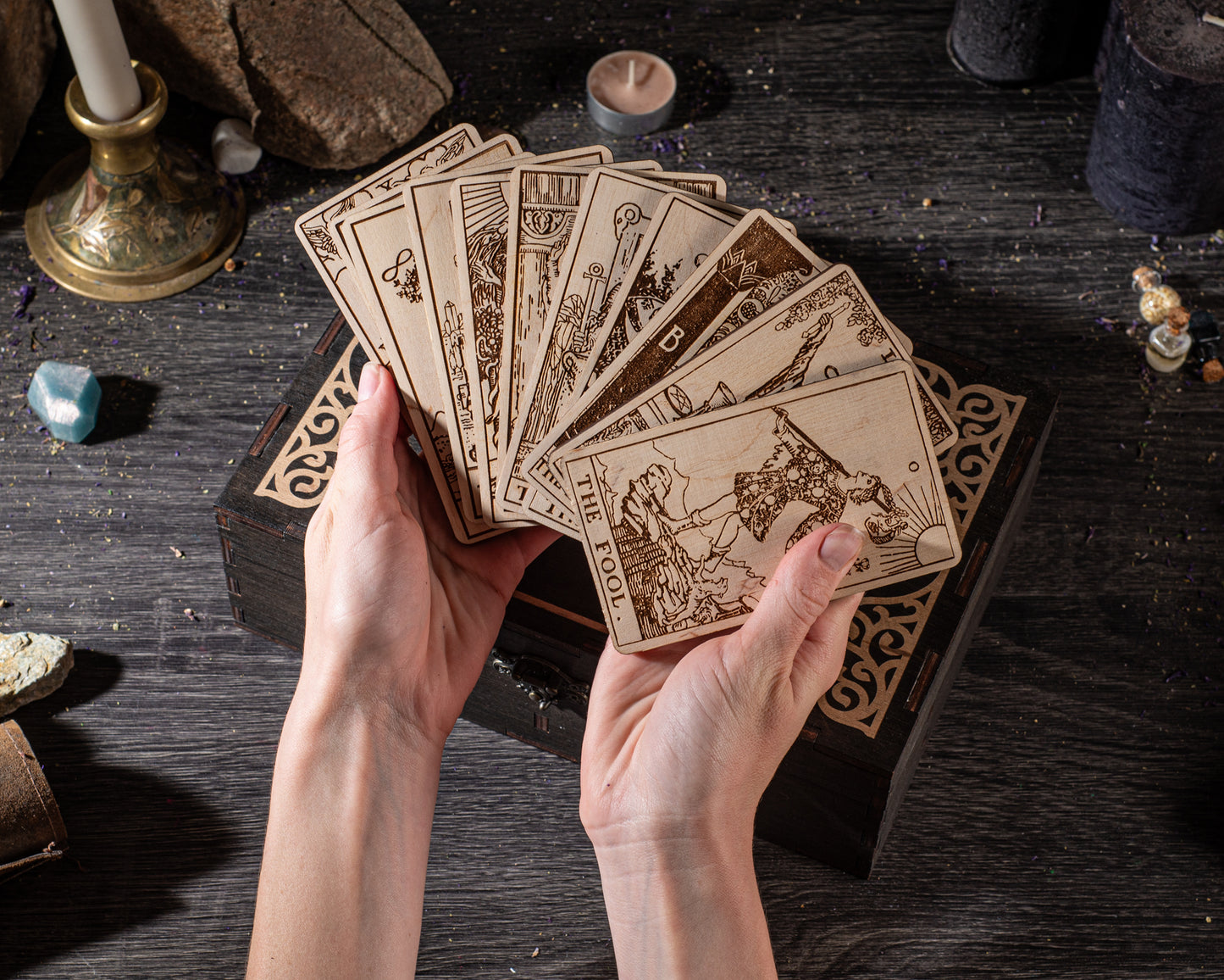 A pair of hands holding a deck of tarot cards on a wooden surface.