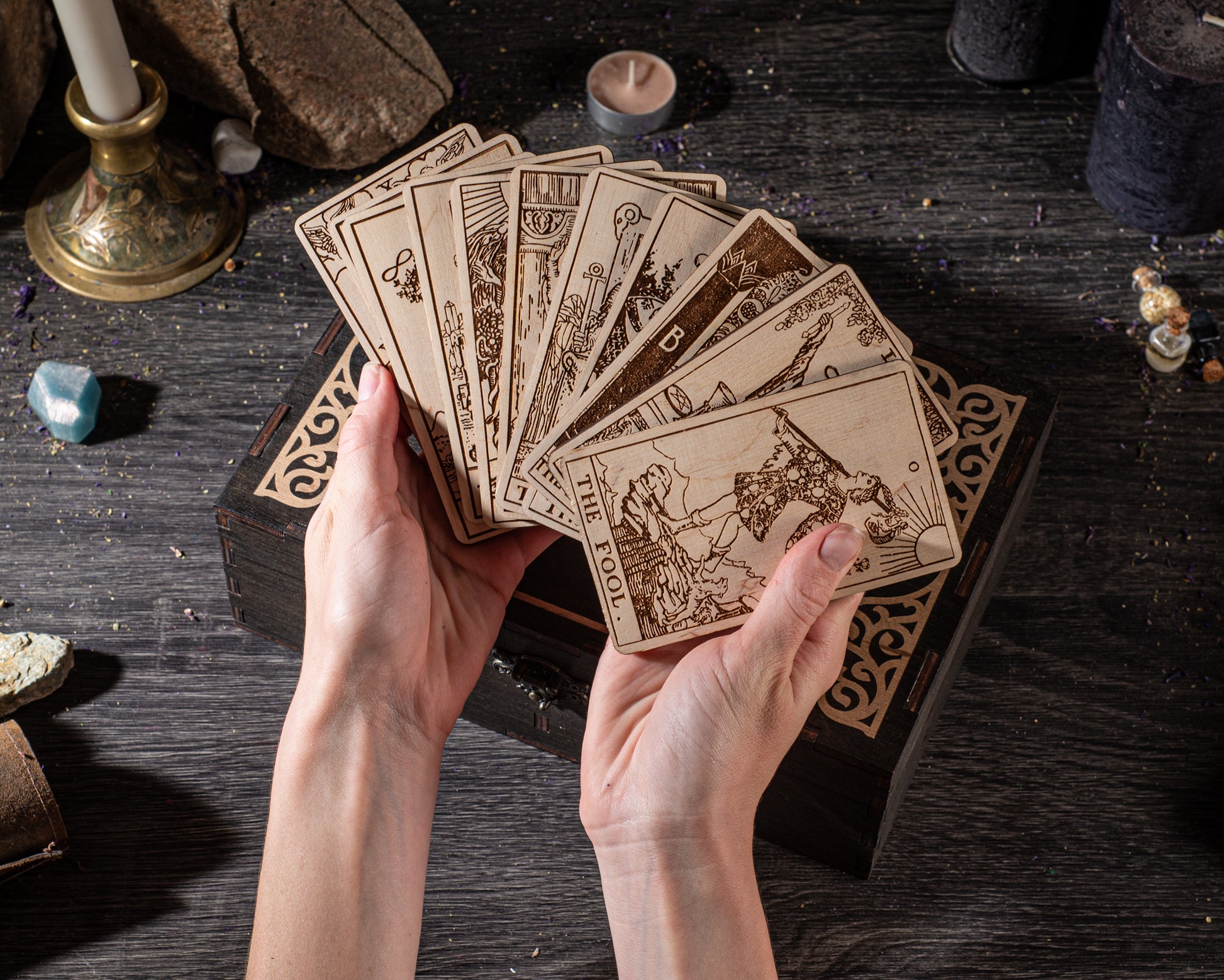 A pair of hands holding a deck of tarot cards on a wooden surface.
