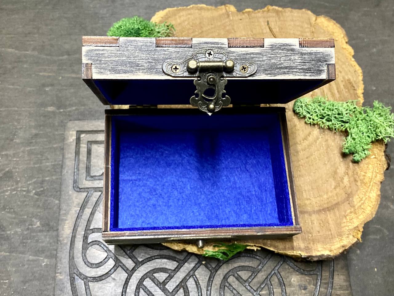 an open wooden box with a blue interior, placed on a wooden surface with a decorative design.