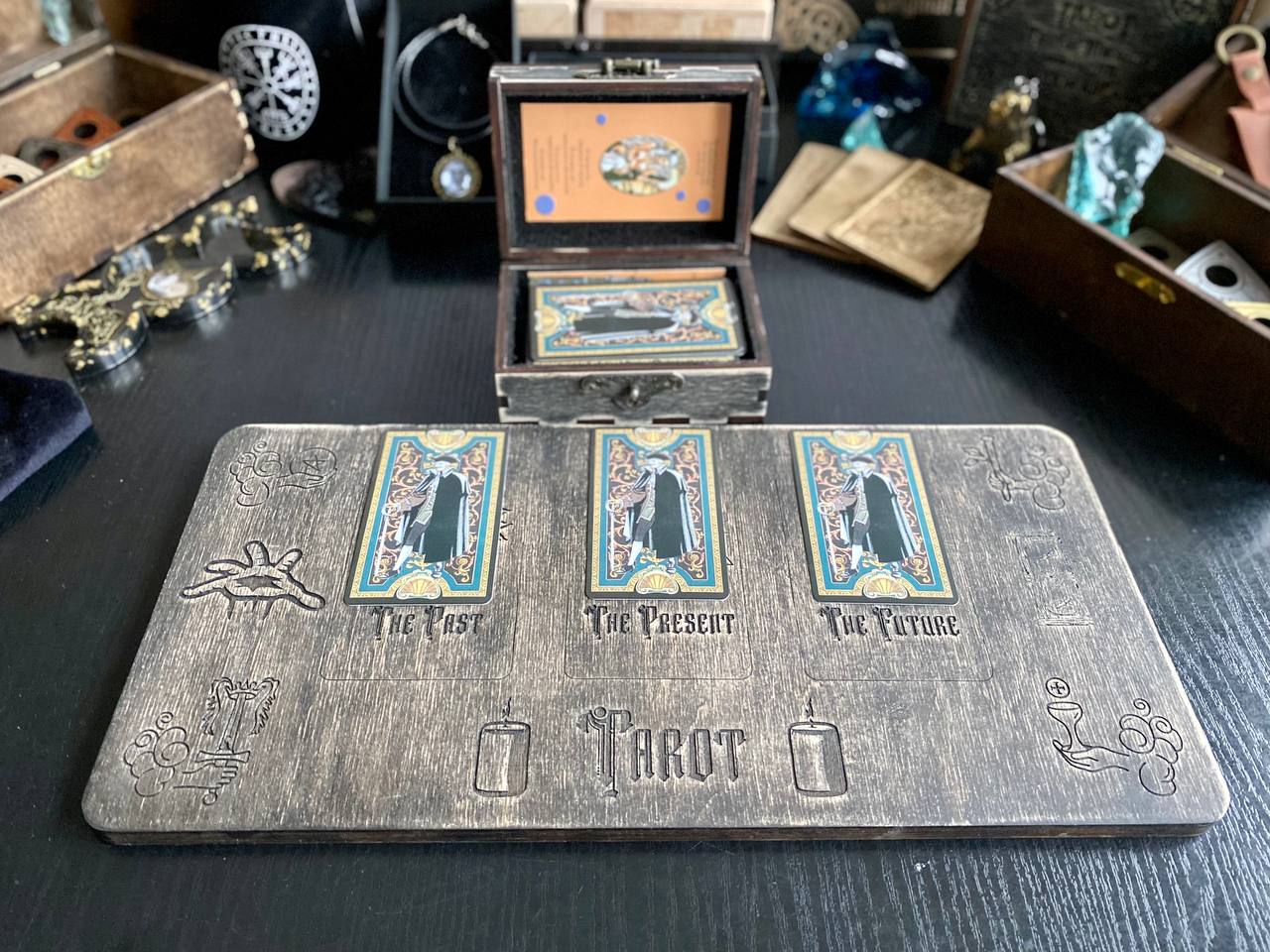 a wooden board with three tarot cards on it, along with a wooden box and various other items on a table.