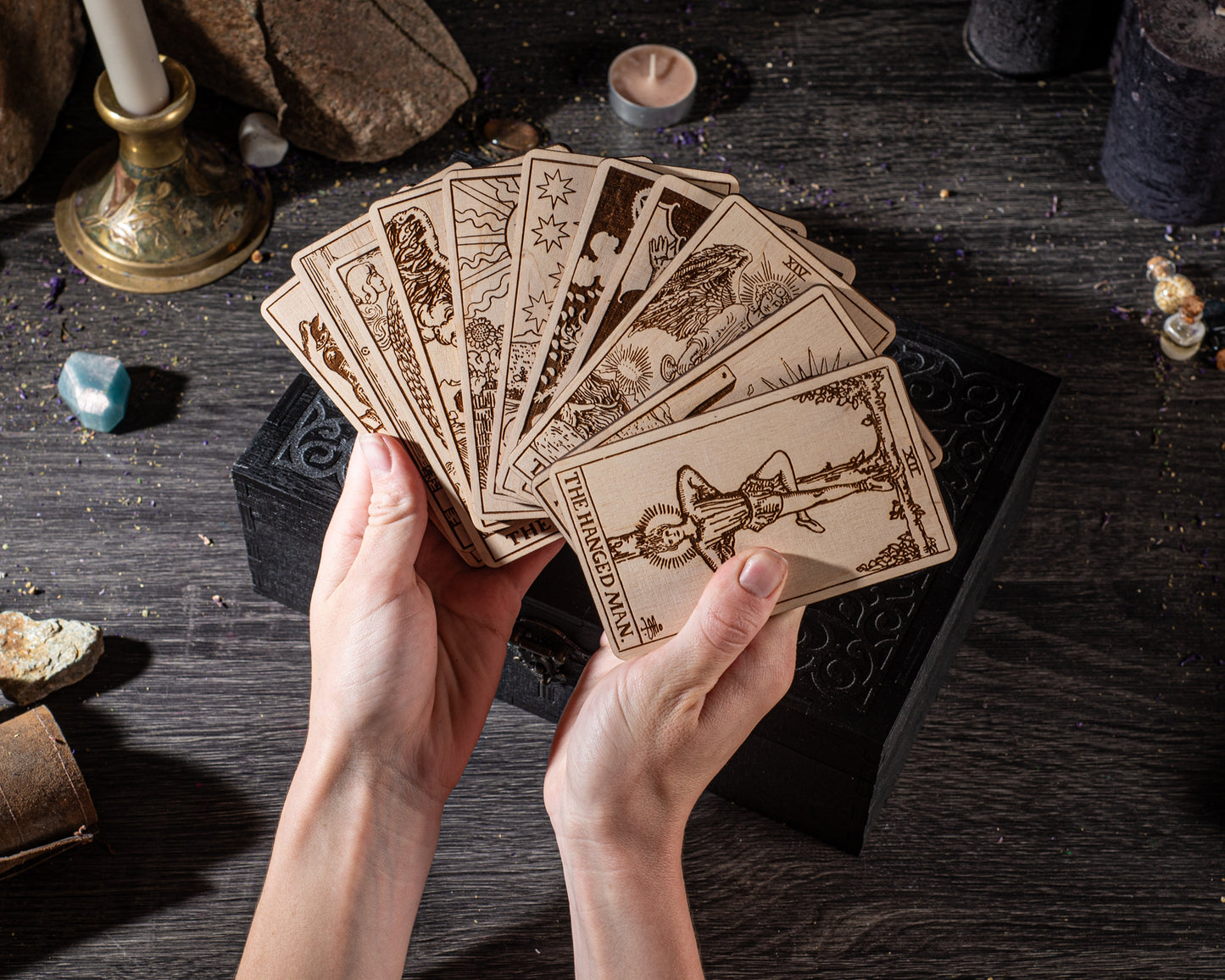 A pair of hands holding a deck of tarot cards on a wooden surface.
