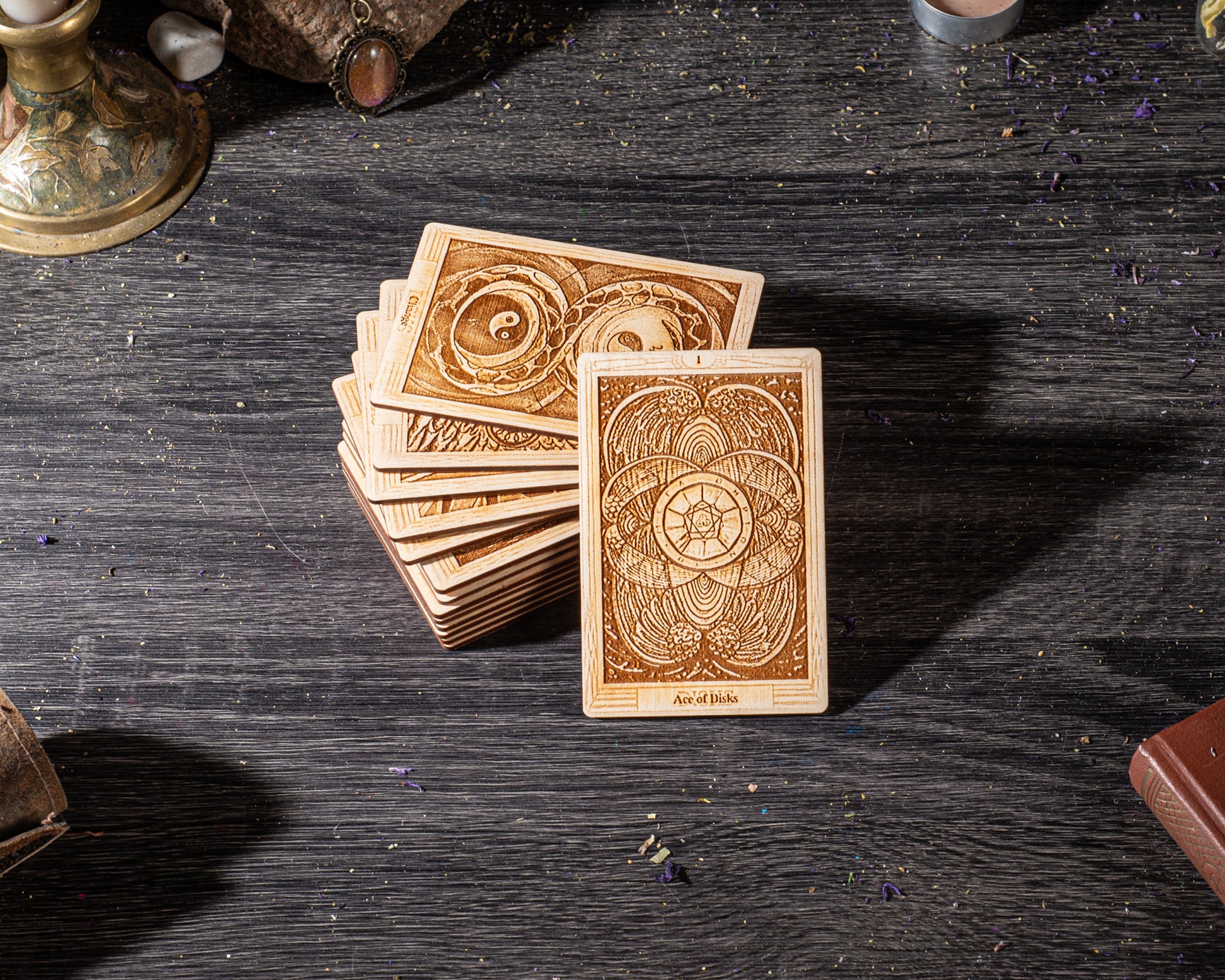 A stack of wooden tarot cards is displayed on a dark wooden surface, with a few small objects scattered around.