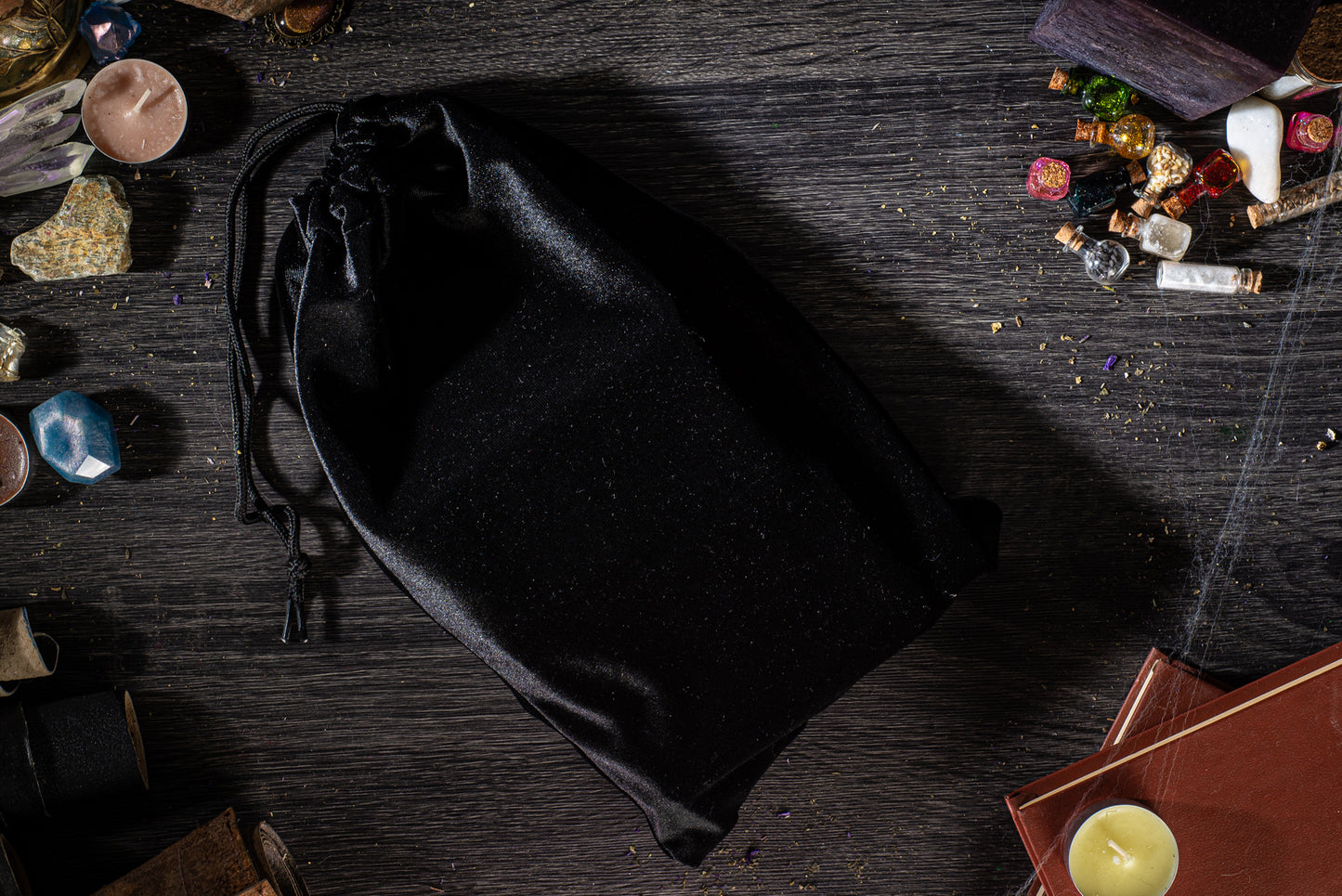 a black satchel placed on a wooden surface, surrounded by various objects such as candles, books, and other miscellaneous items.