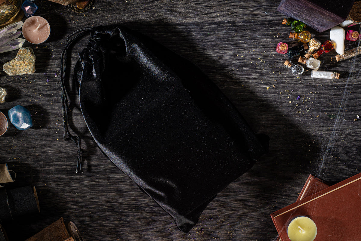 a black satchel placed on a wooden surface, surrounded by various objects such as candles, books, and other miscellaneous items.