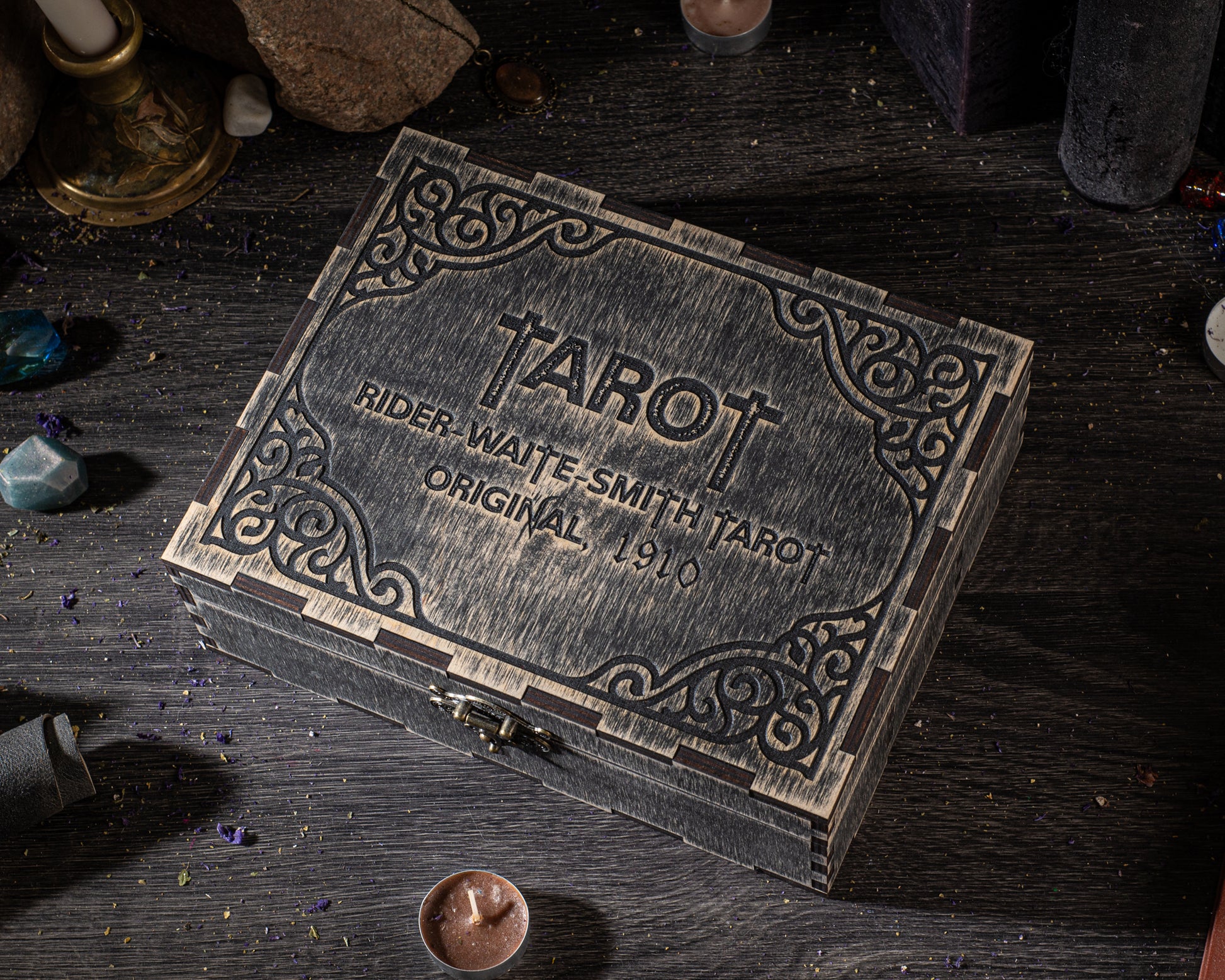A wooden box with a decorative border, labeled "TAROT" and "RIDER-WAITE-SMITH TAROT ORIGINAL 1910", sits on a wooden surface surrounded by various objects.