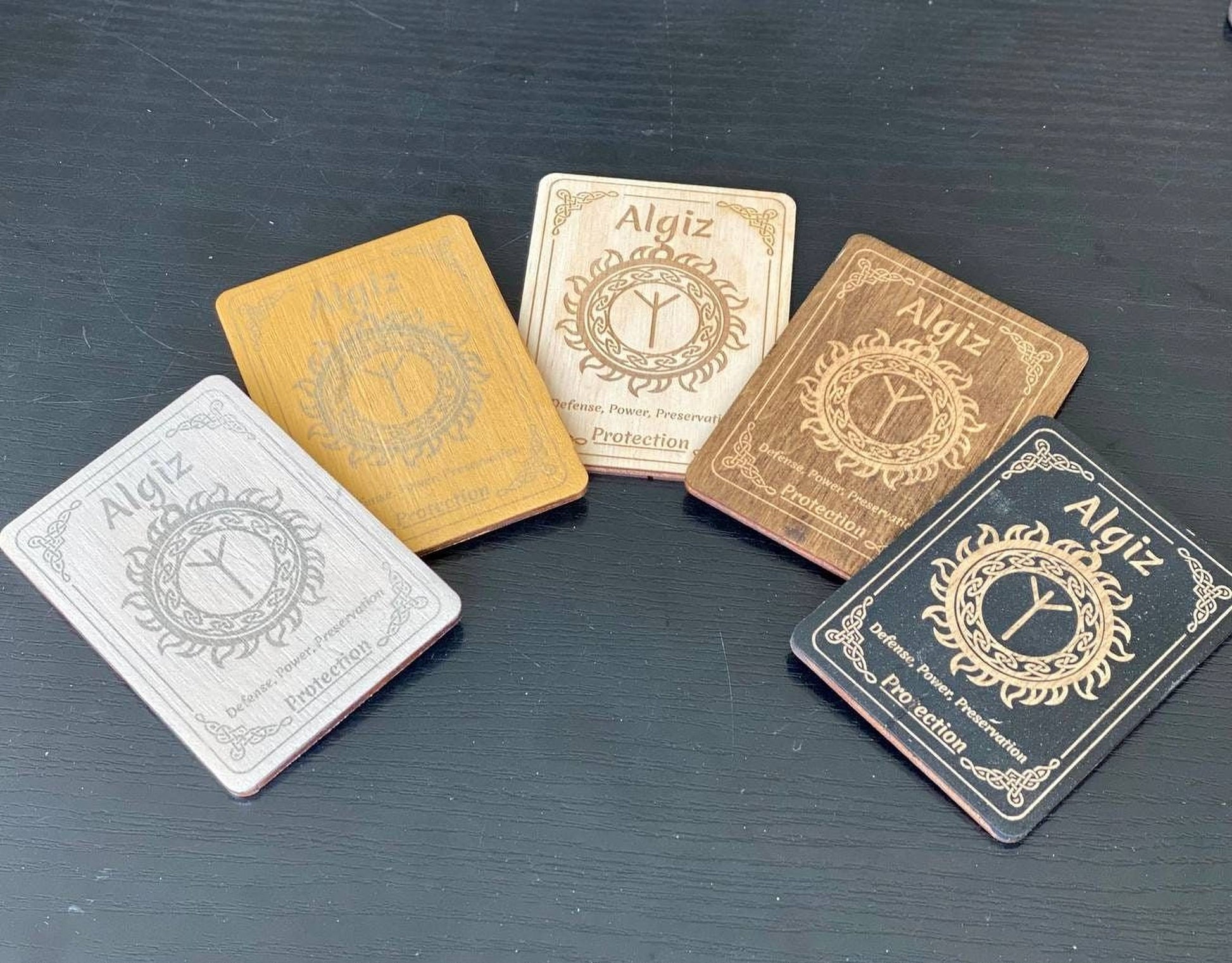 five wooden coasters with the name "Algiz" printed on them, arranged in a circular pattern on a dark surface.