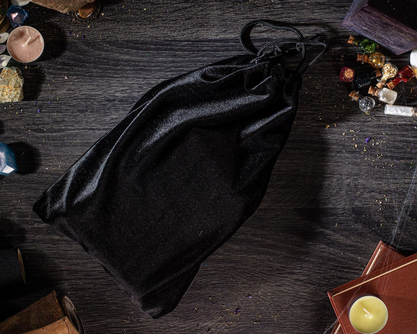 a black velvet bag placed on a wooden surface, surrounded by various objects such as candles, books, and other items.
