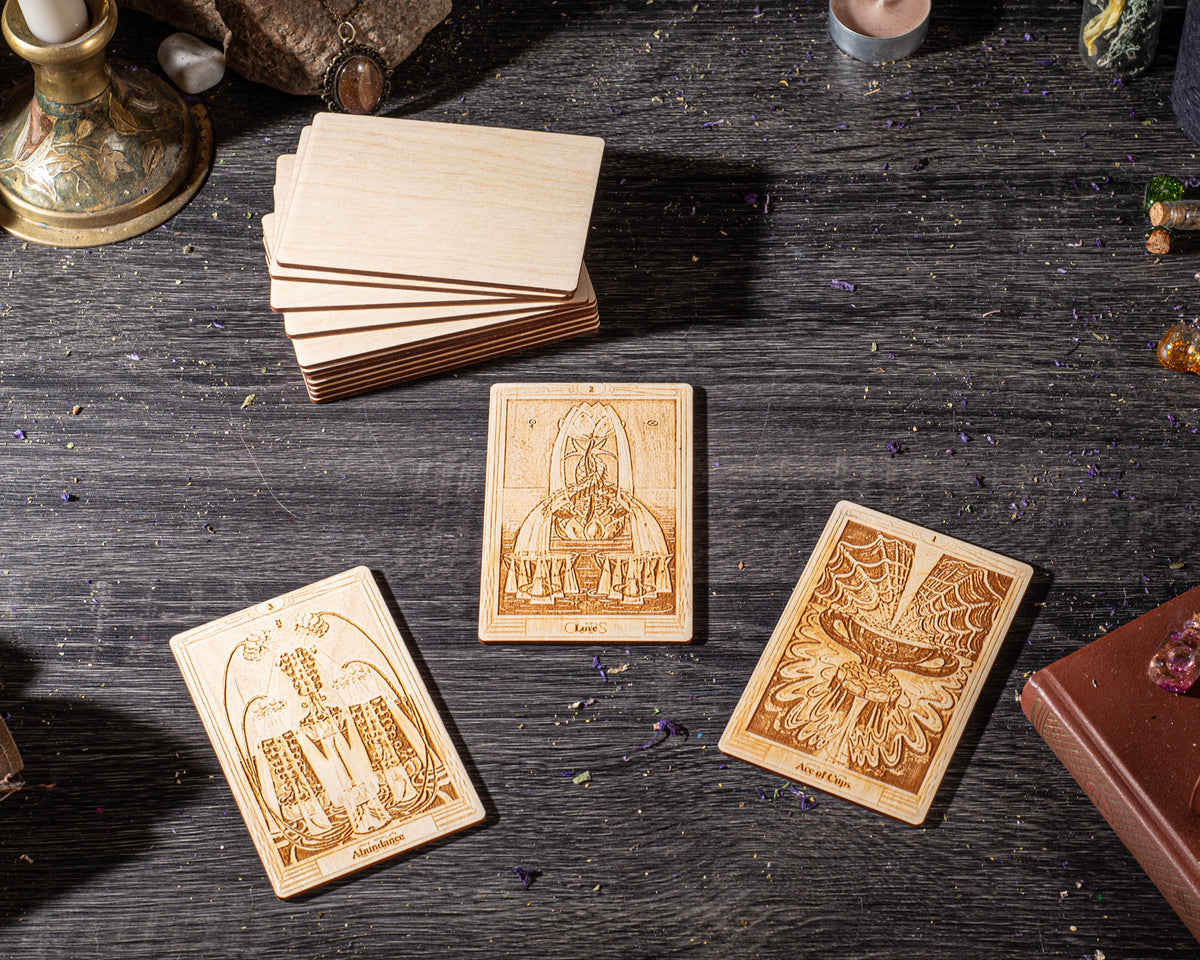 three wooden tarot cards with intricate designs, placed on a wooden surface alongside various objects such as a candle, a book, and some small figurines.