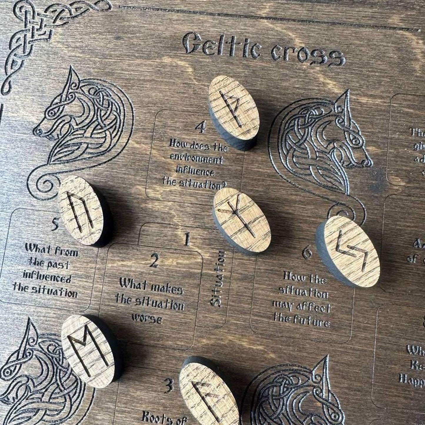 a wooden board with various symbols and text related to Celtic cross, including a wolf and a wolf's head. There are also several wooden pieces with symbols on them, which appear to be part of a game or puzzle.