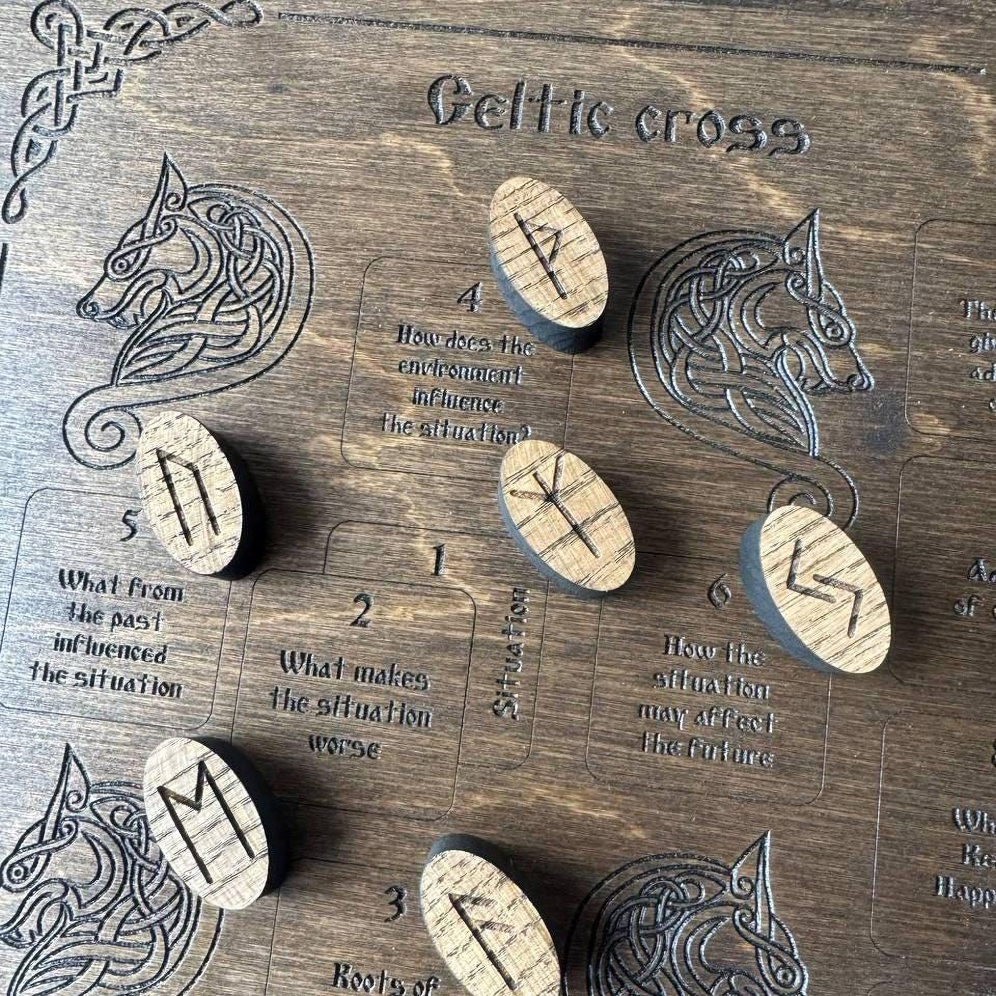 a wooden board with various symbols and text related to Celtic cross, including a wolf and a wolf's head. There are also several wooden pieces with symbols on them, which appear to be part of a game or puzzle.