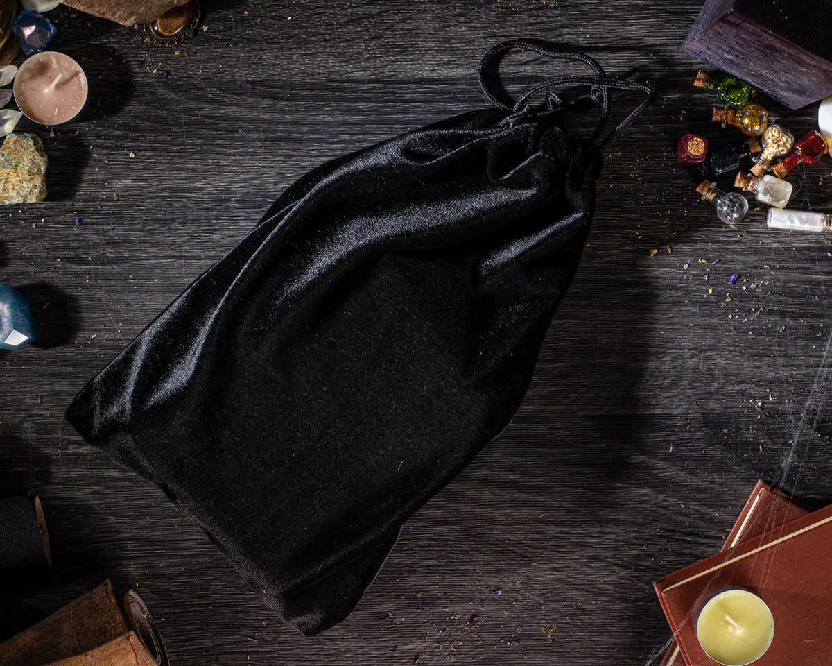 a black velvet bag placed on a wooden surface, surrounded by various objects such as candles, books, and other miscellaneous items.