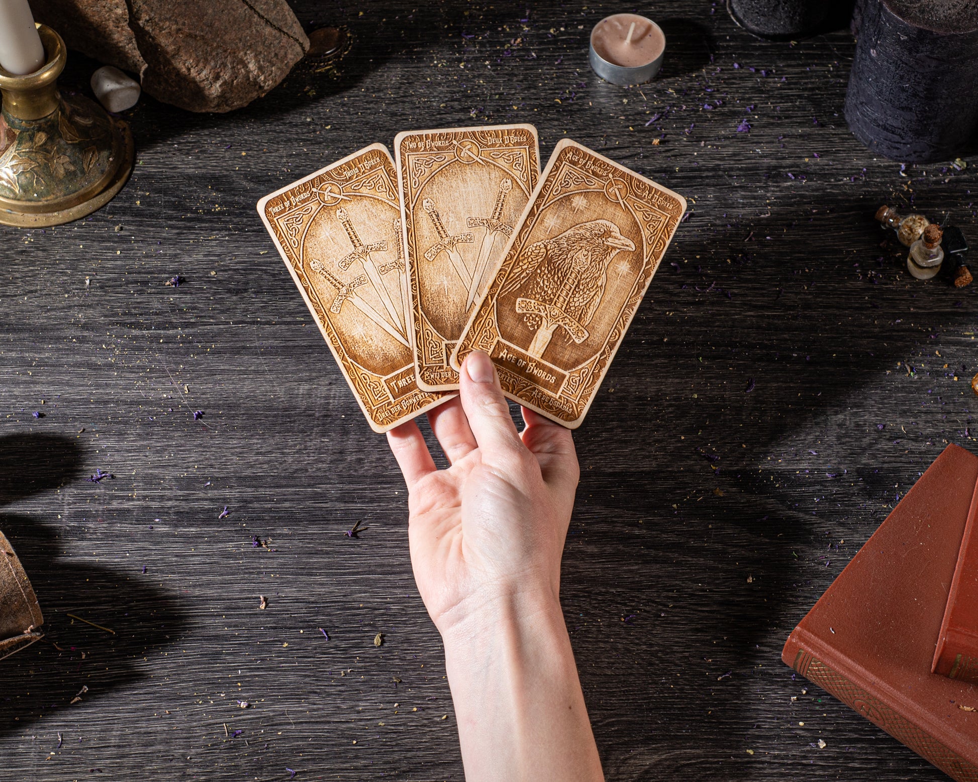 A hand is holding three wooden cards with intricate designs, placed on a dark wooden surface.