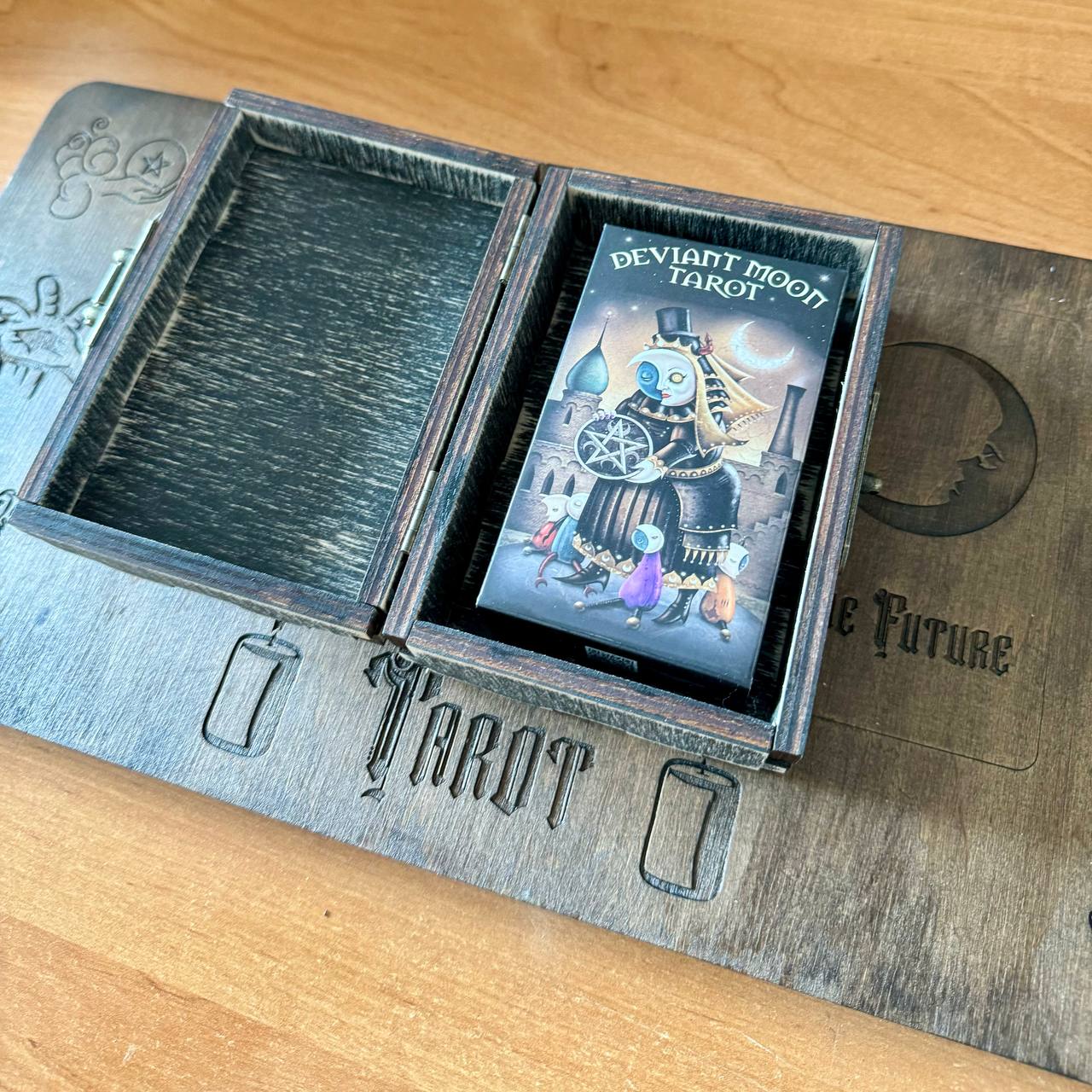 a tarot card box with a printed design on the lid and a wooden board with embossed text below it.