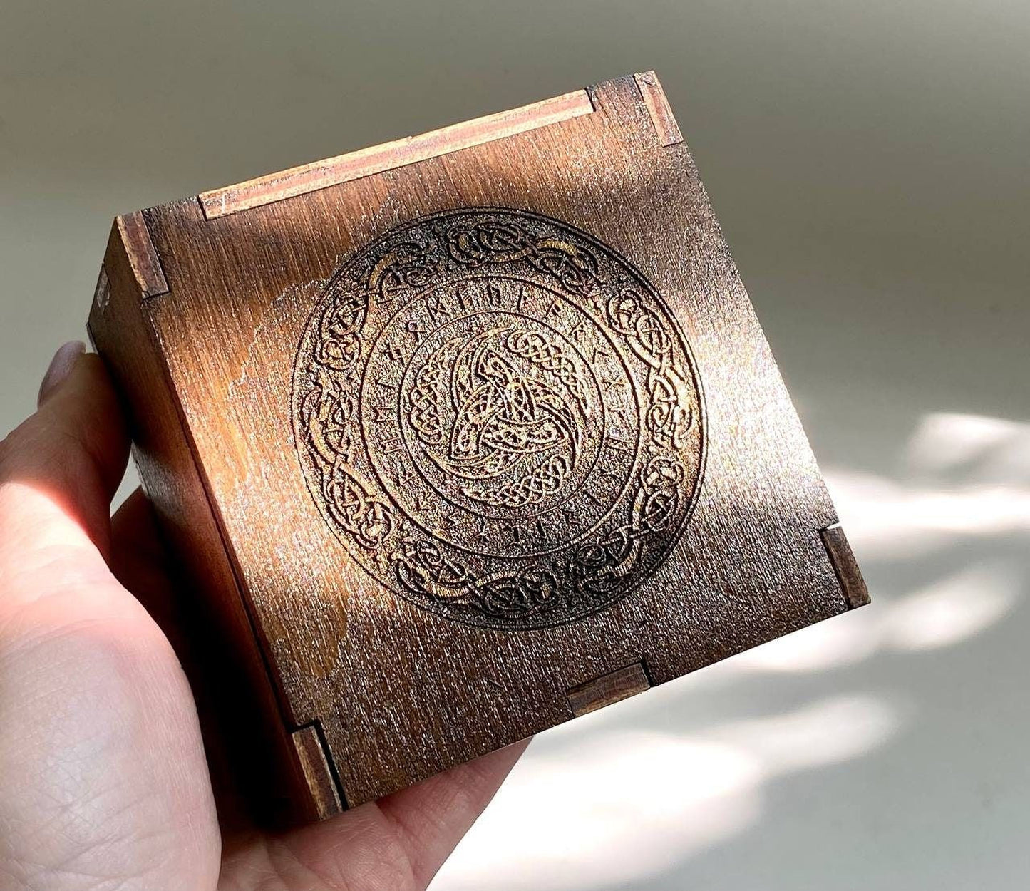 A hand is holding a wooden box with an intricate engraved design on its surface.
