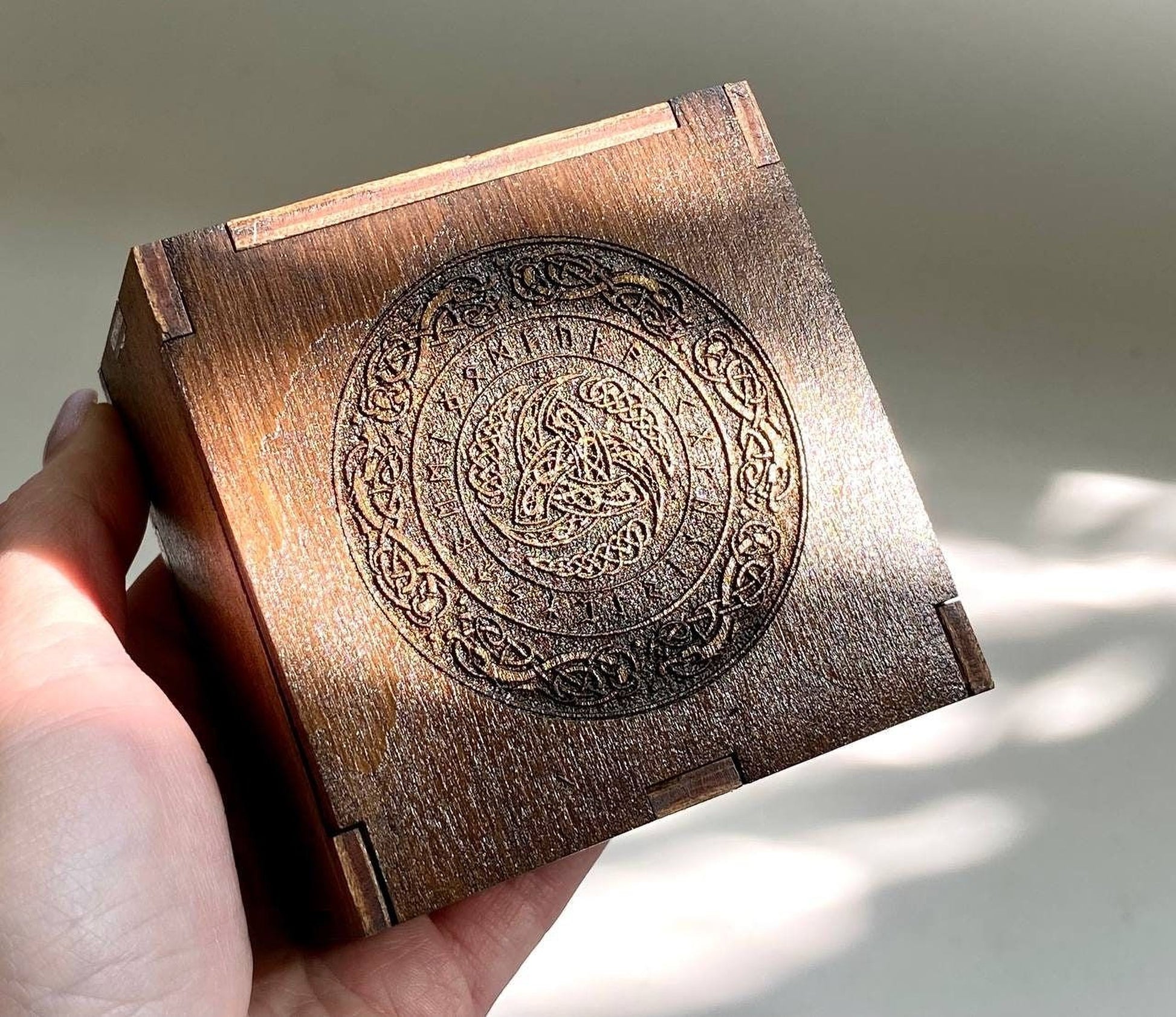 A hand is holding a wooden box with an intricate engraved design on its surface.