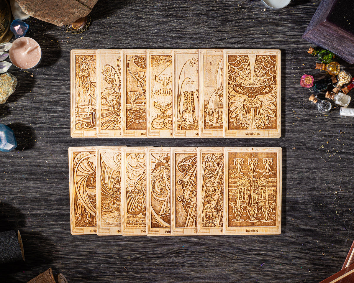 A collection of wooden tarot cards arranged on a dark wooden surface, with various objects such as candles, gemstones, and other items scattered around them.