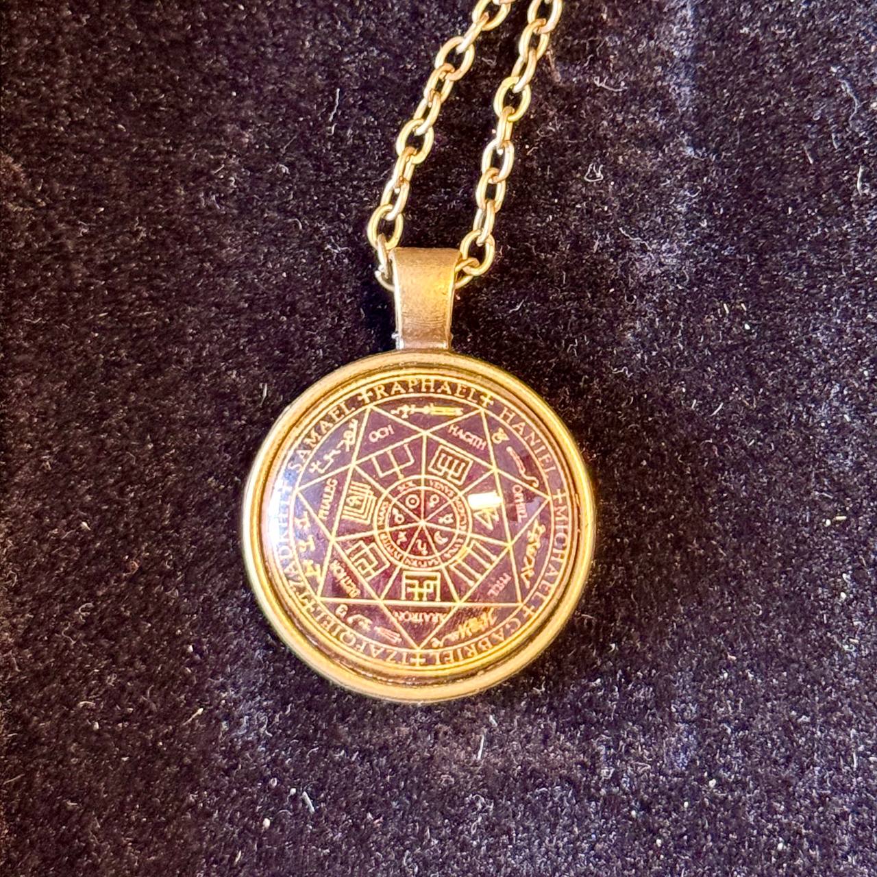 A gold-colored pendant necklace with a circular medallion featuring a complex design and text.