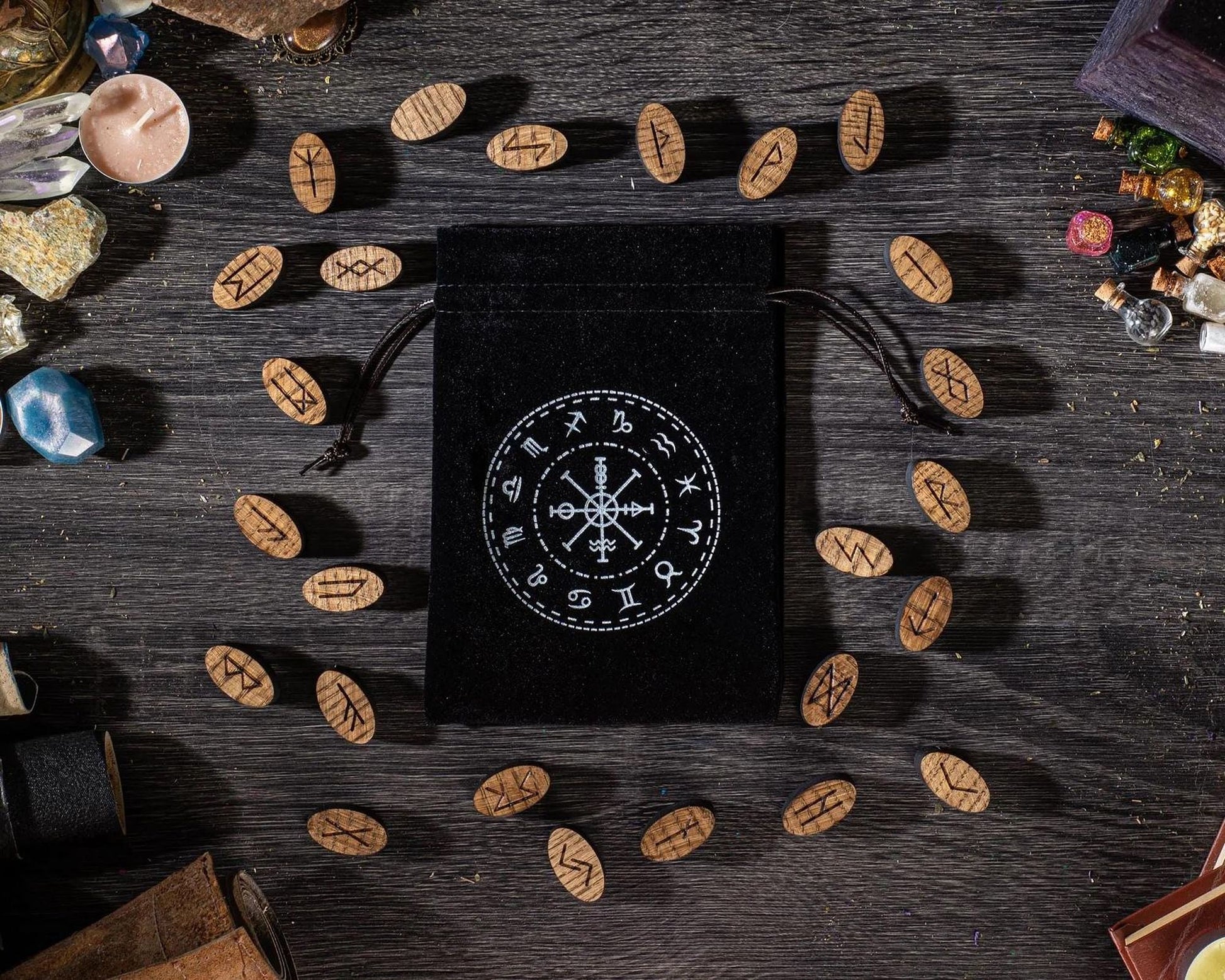 a black pouch with a white design on it, surrounded by various objects such as wooden beads, crystals, and other items on a wooden surface.