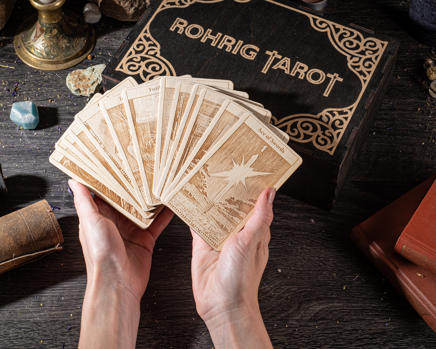 A person's hands holding a deck of wooden tarot cards, with a "Rohrig Tarot" box visible in the background.