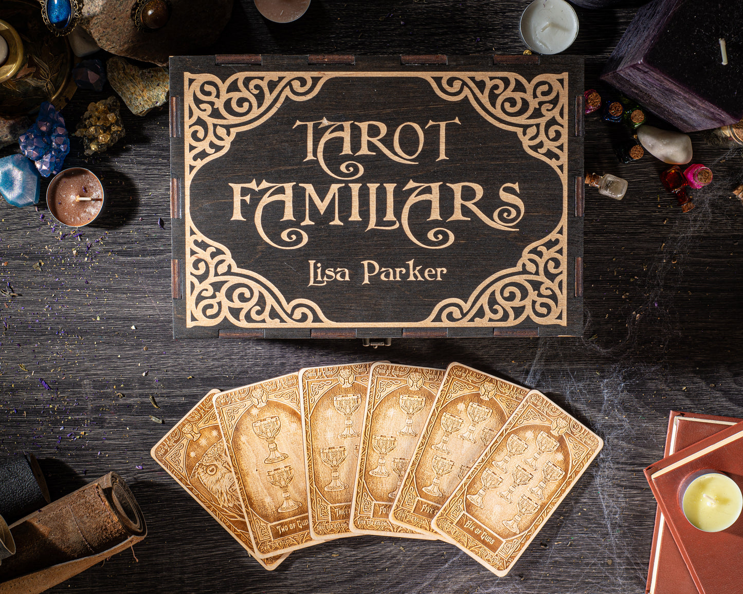 a wooden box with the title "Tarot Familiars" and the name "Lisa Parker" on it, along with a set of tarot cards and various other items such as candles, gemstones, and books.