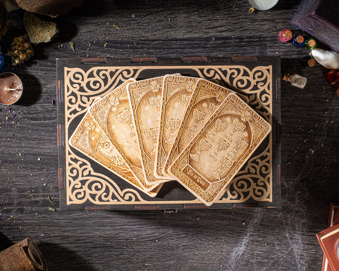 A wooden box with a decorative border, containing a fan of ornately carved wooden cards, is placed on a dark wooden surface.
