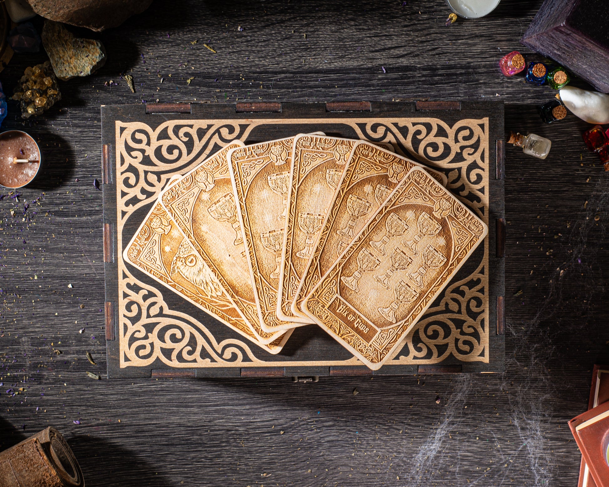 A wooden box with a decorative border, containing a fan of ornately carved wooden cards, is placed on a dark wooden surface.