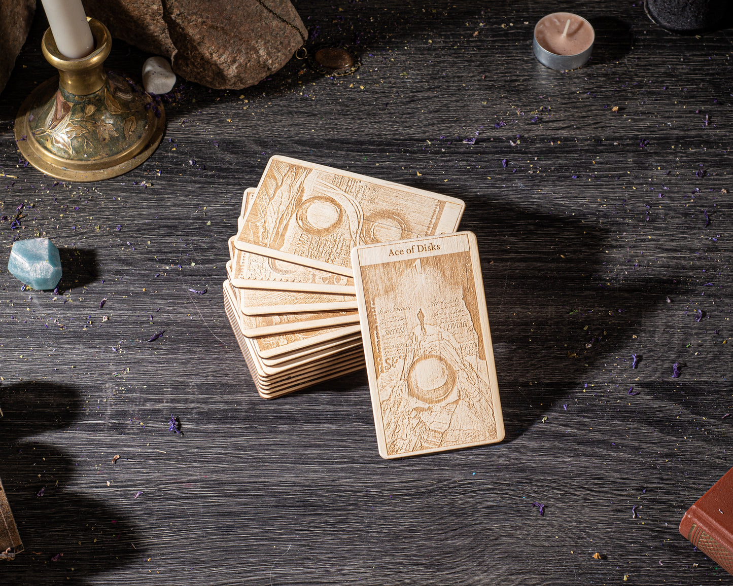 A deck of playing cards is displayed on a wooden surface, with a candle and various other objects in the background.