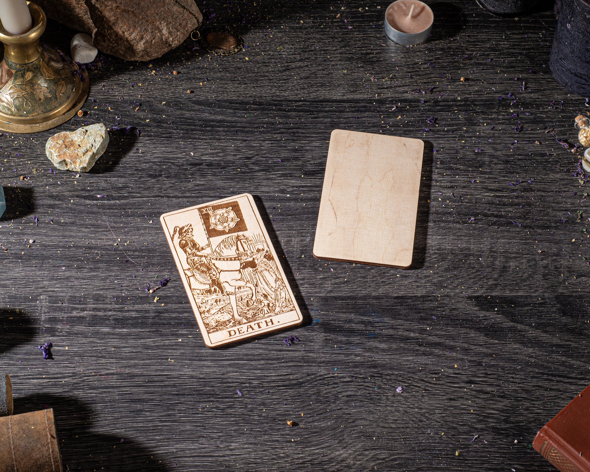a tarot card with the word "DEATH" on it, along with a wooden card holder and some candles on a dark wooden surface.