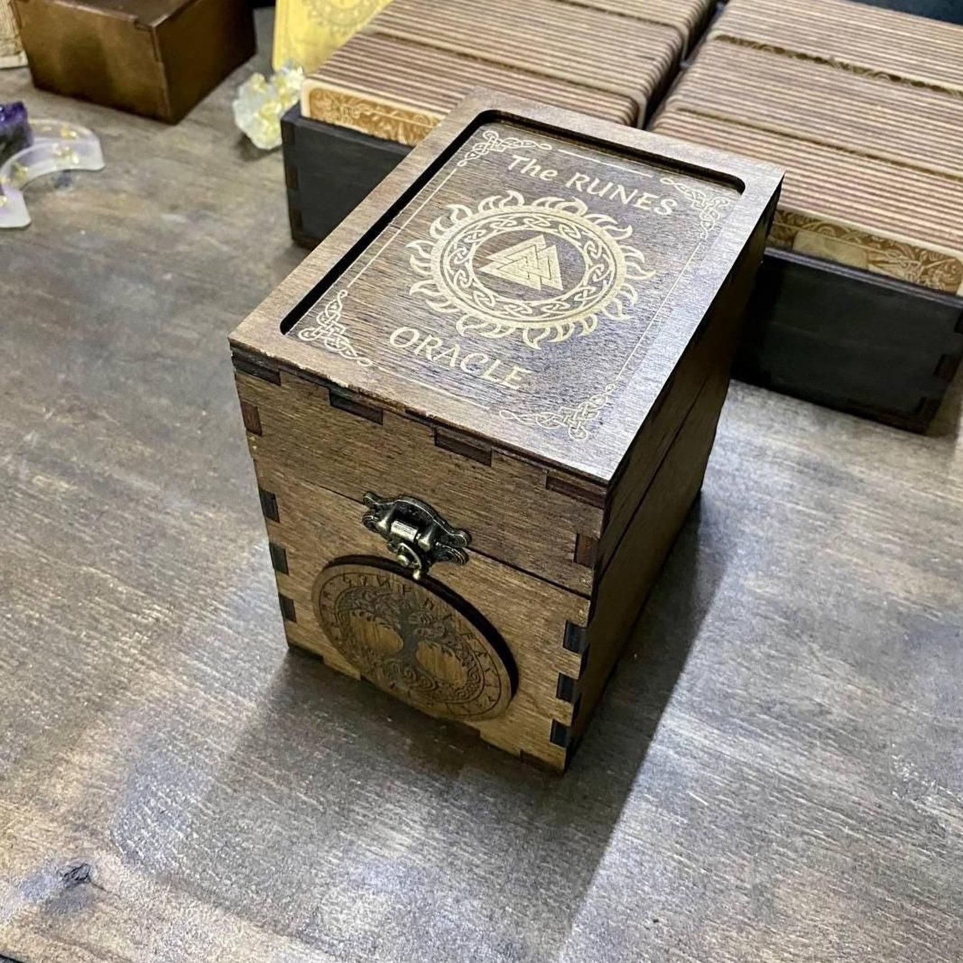 A wooden box with a metal clasp and a tree-like emblem on it, sitting on a wooden surface.
