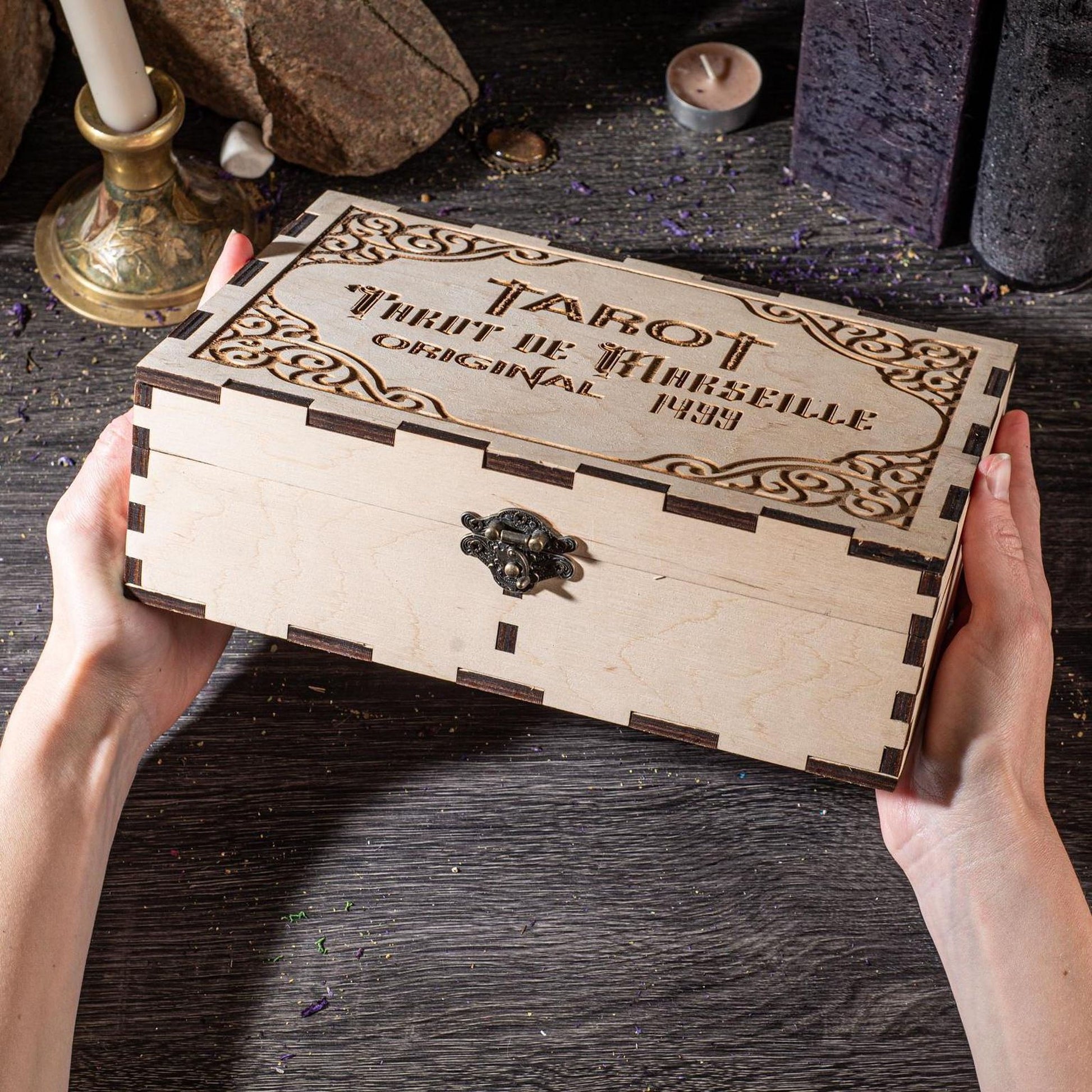 A person's hands are holding a wooden box with the text "TAROT" and "ORIGINAL" engraved on it, along with a key-like object.