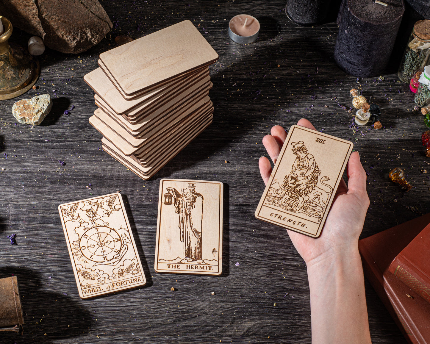 A hand holding a wooden tarot card with the text "STRENGTH" on it, surrounded by other wooden cards and objects on a dark wooden surface.