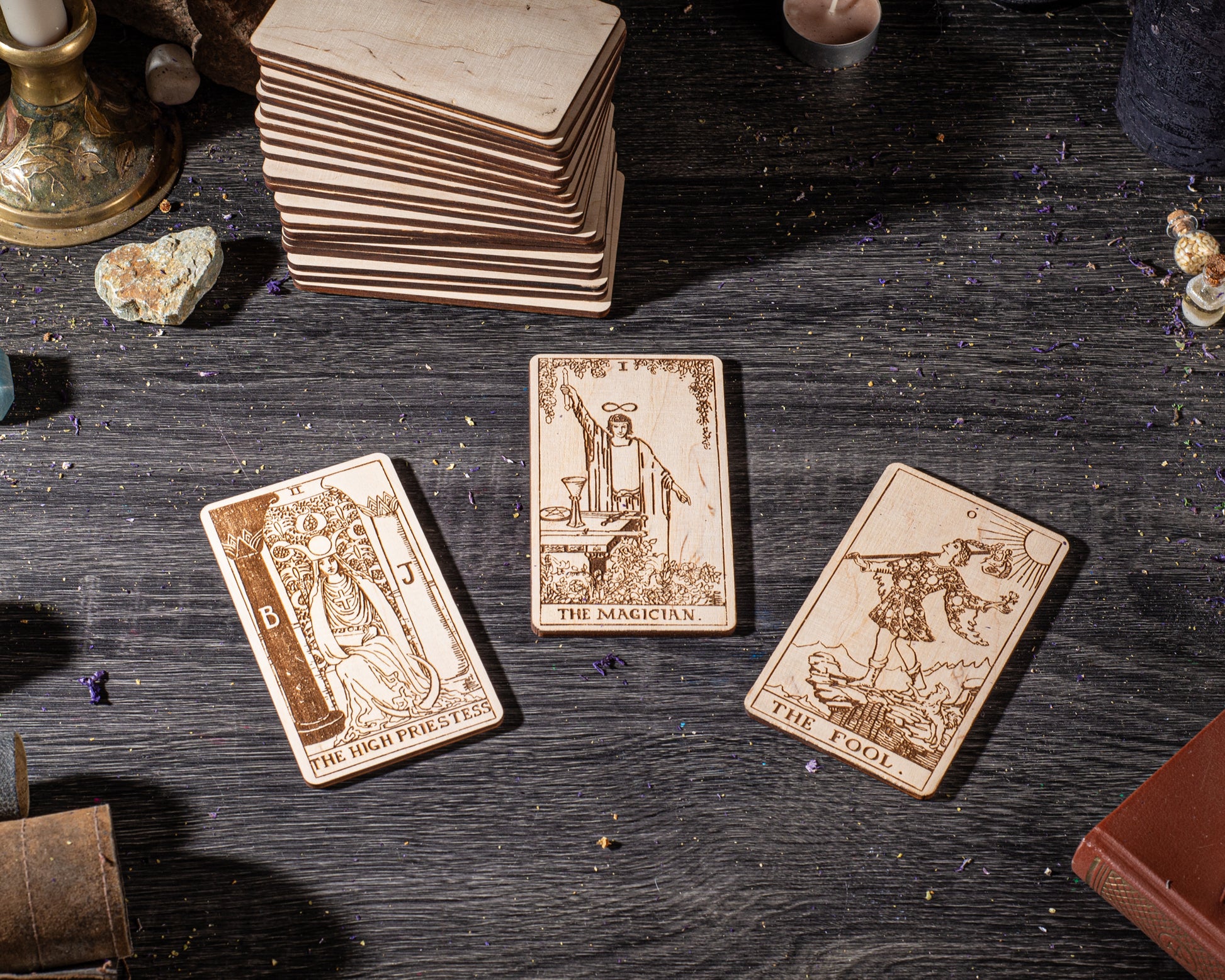 three wooden tarot cards with intricate designs, placed on a wooden surface alongside various objects such as crystals, candles, and a book.