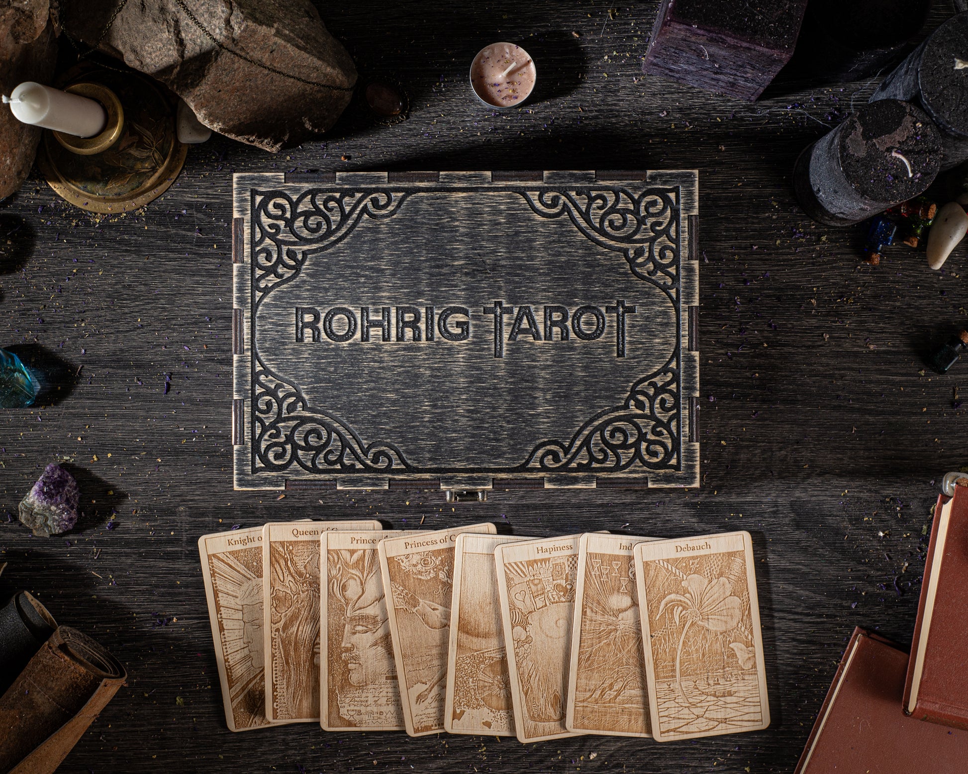 a wooden box with the name "Rohrig Tarot" carved into it, surrounded by various tarot cards and other objects on a dark wooden surface.