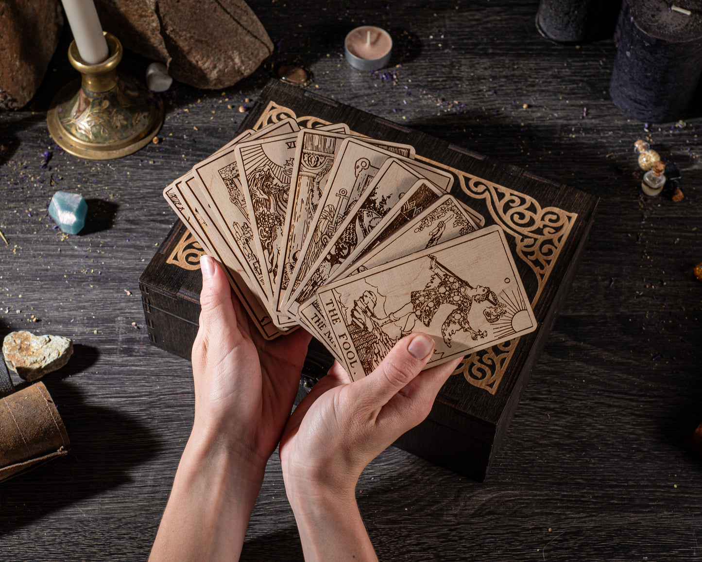 A pair of hands holding a deck of tarot cards on a wooden surface.