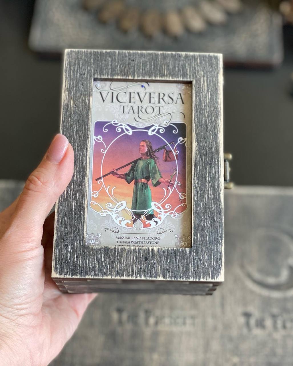 A hand is holding a small wooden box with a tarot card inside.