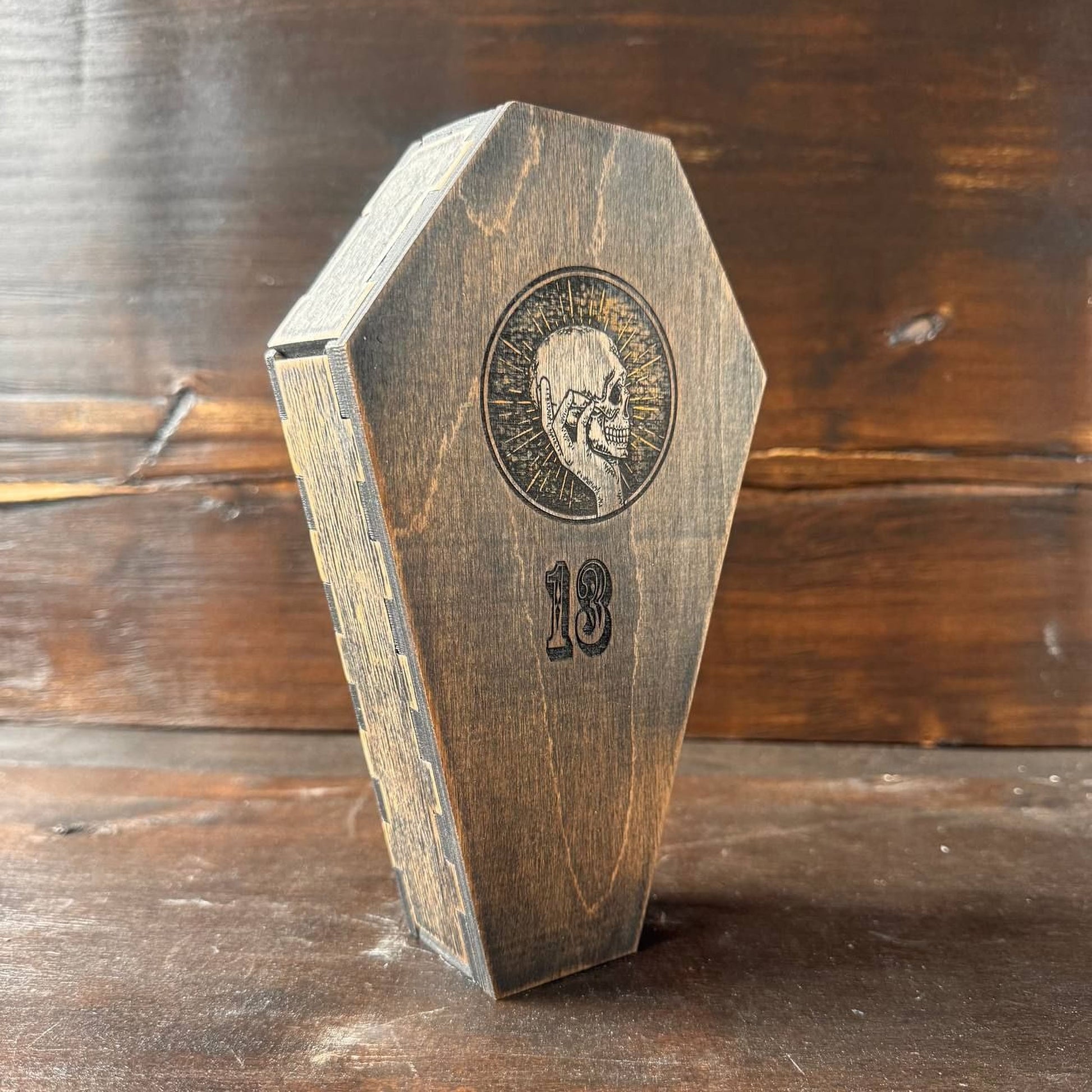 A wooden box with a skull design and the number 18 printed on it, placed on a wooden surface.