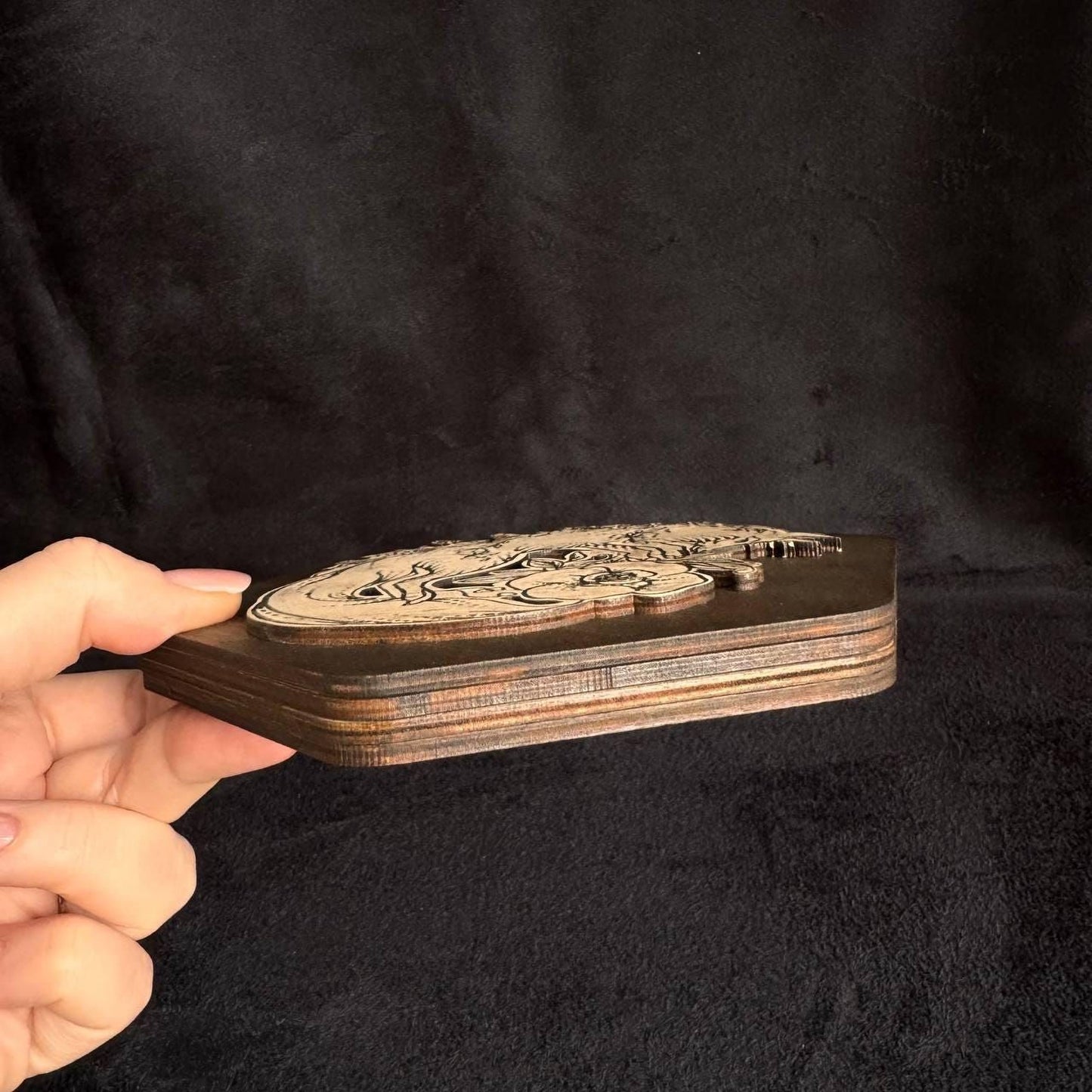 A hand is holding a wooden object with a carved design on it against a dark background.