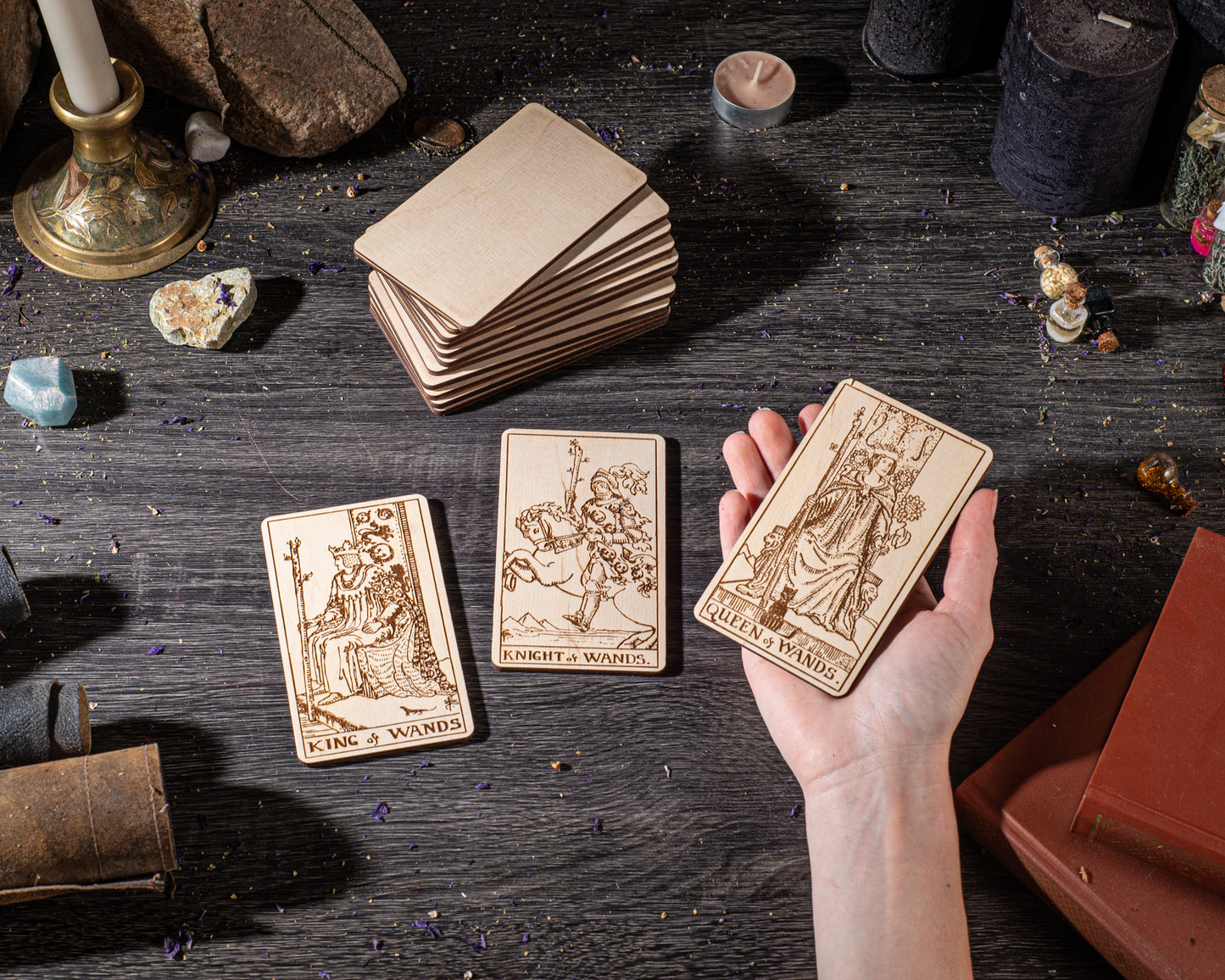 A hand is holding three wooden tarot cards with illustrations on them, placed on a dark wooden surface.