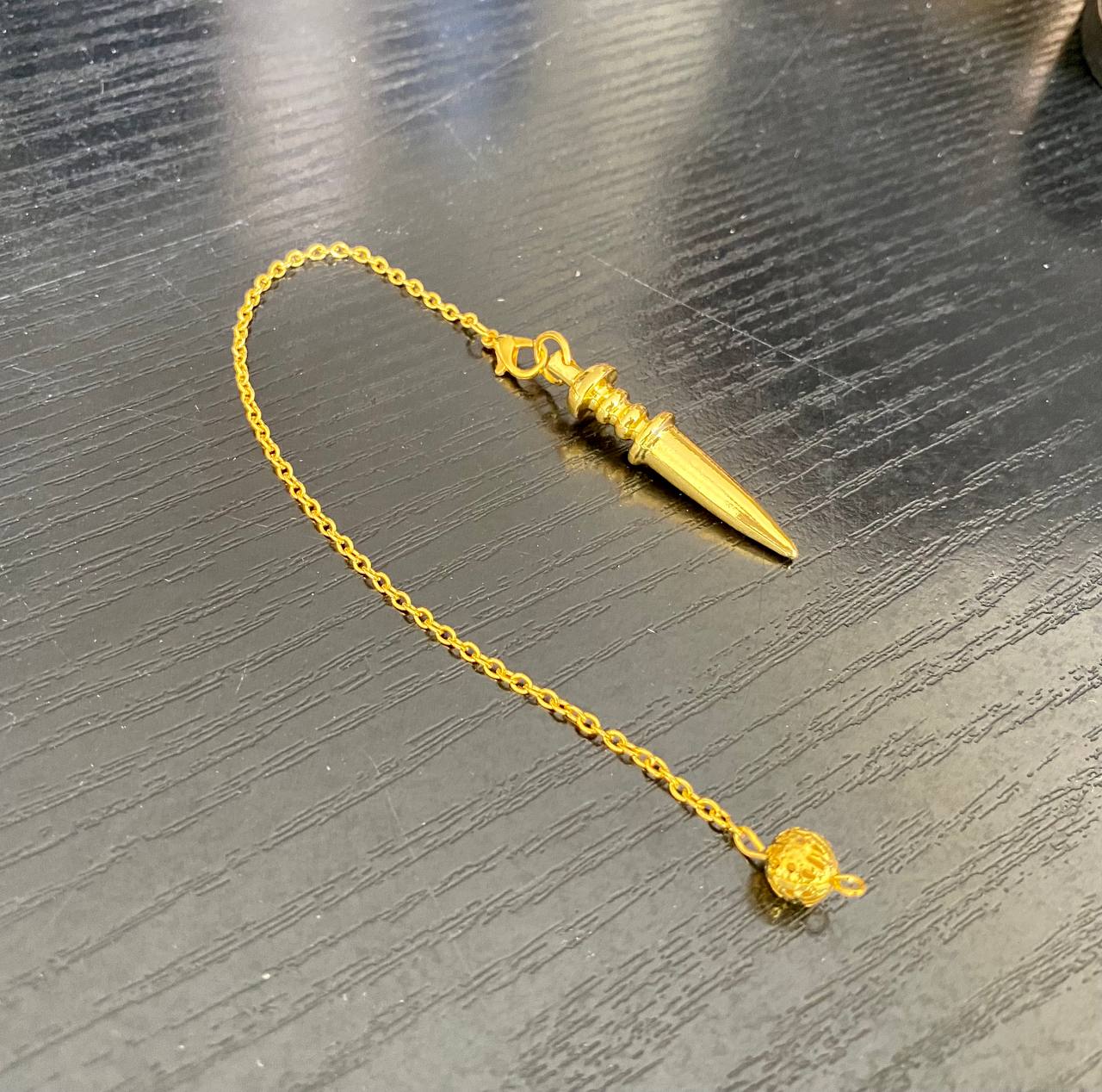 A gold pendulum with a small ball at the end is lying on a wooden surface.