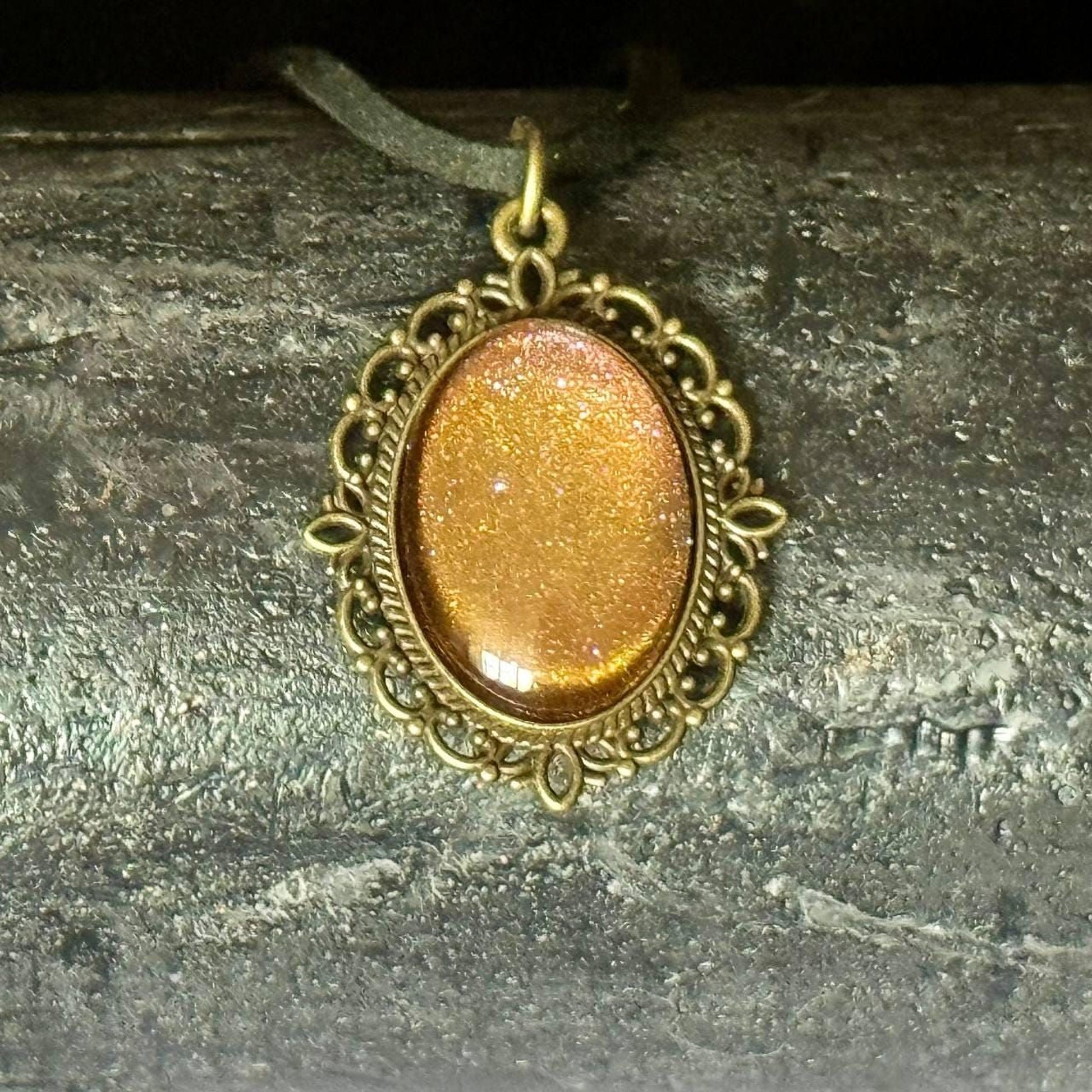 A decorative pendant with a gold-colored stone or gemstone, hanging from a chain or cord.