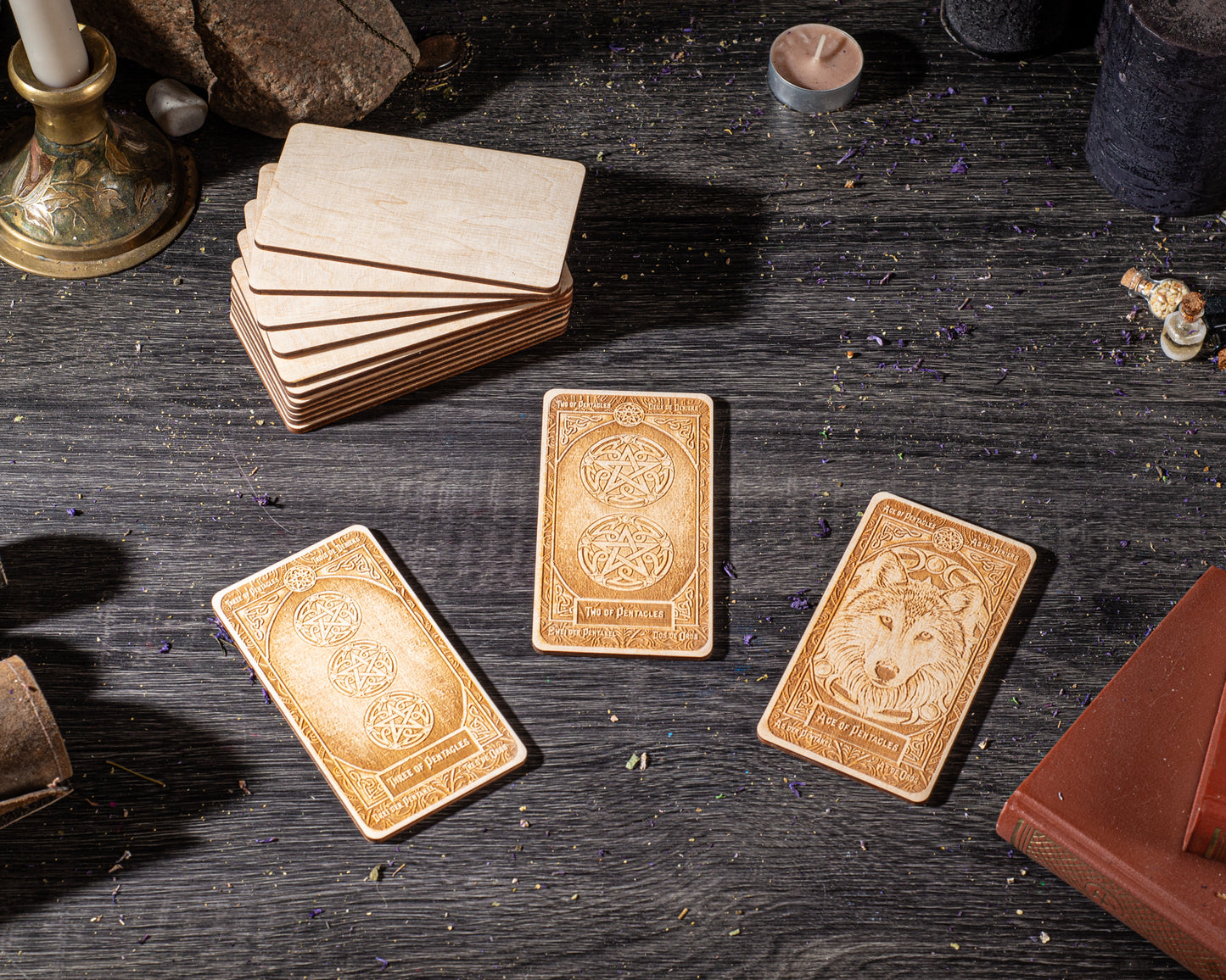three wooden tarot cards with intricate designs, arranged on a wooden surface alongside various objects such as candles, books, and crystals.