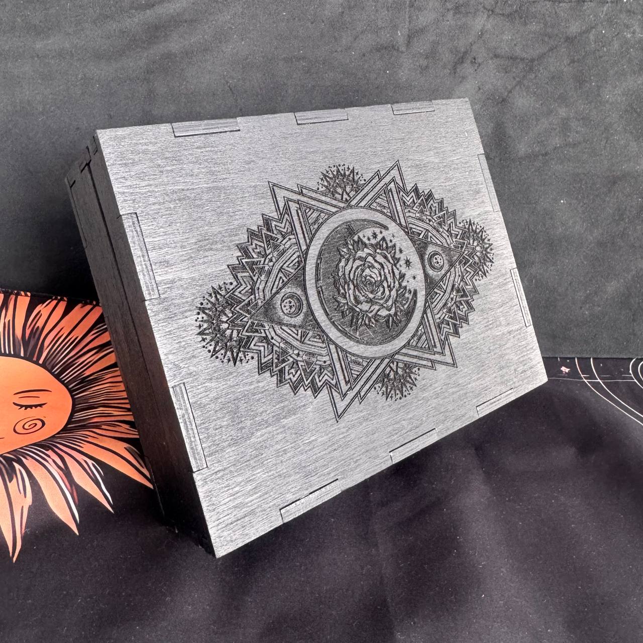 A wooden box with an intricate design featuring a flower and geometric patterns, placed on a black surface.