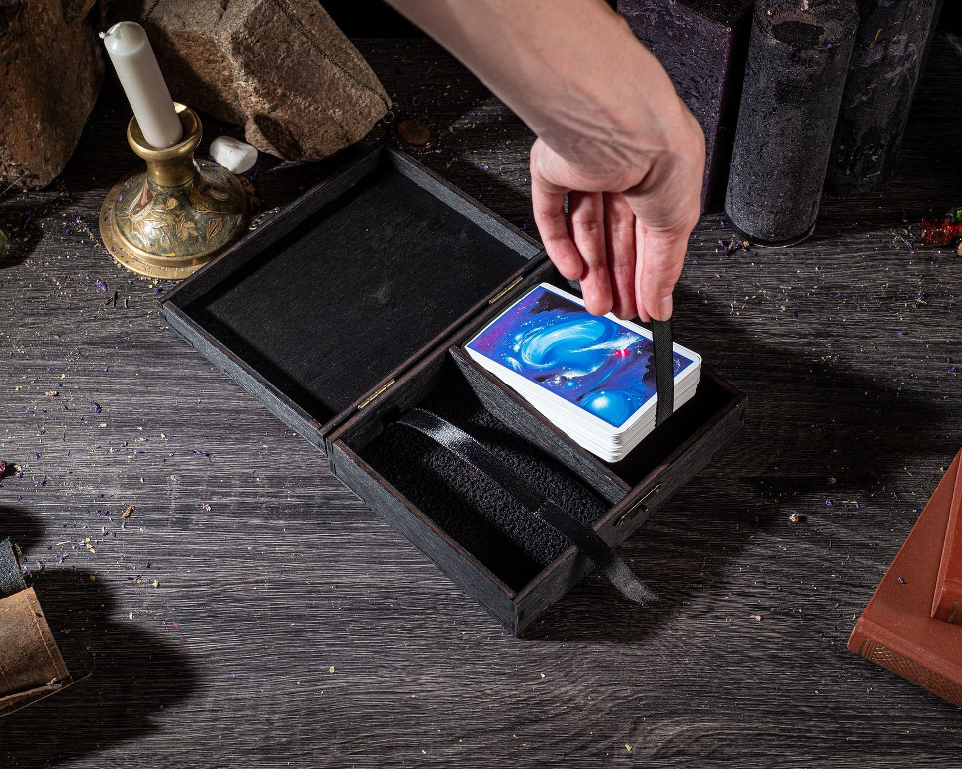 A hand is holding a deck of playing cards, which are placed inside a wooden box on a wooden surface.