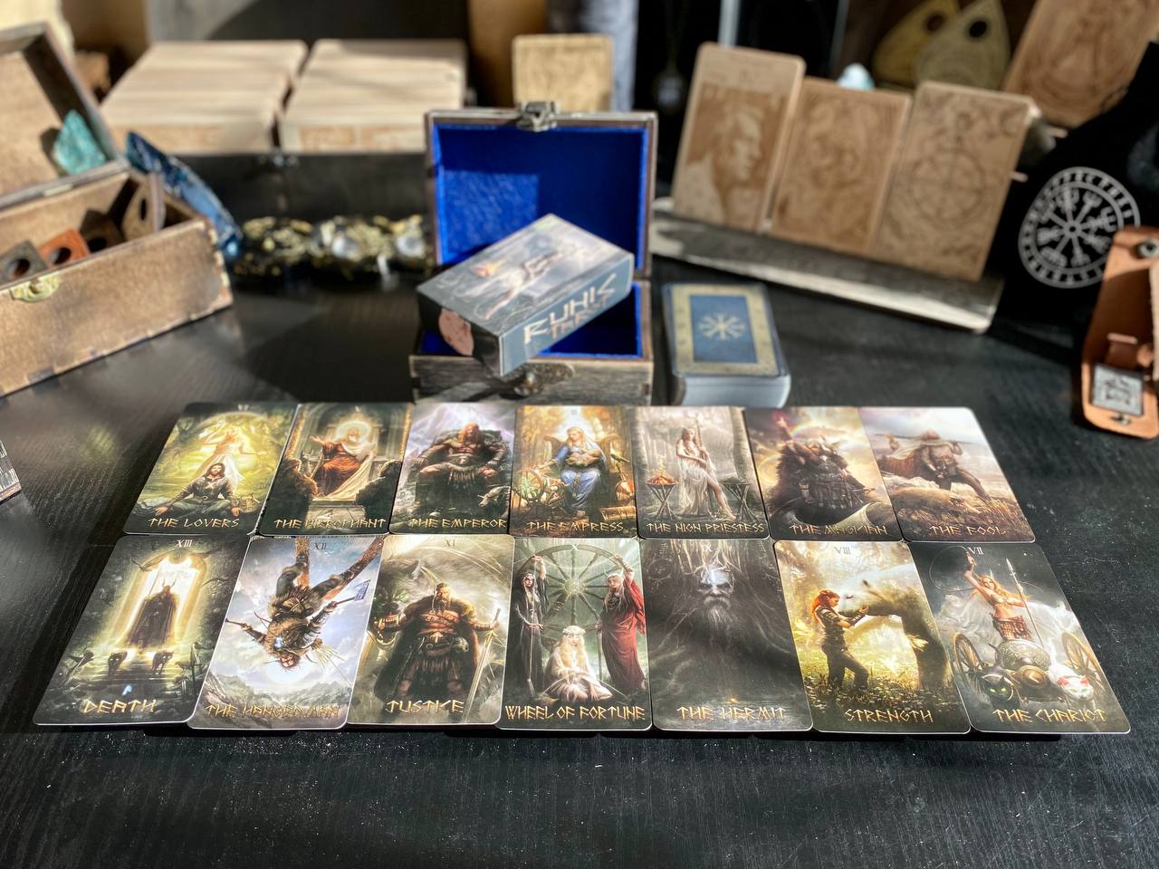 a collection of tarot cards arranged on a table, with a blue box containing additional cards and a wooden box with a carved design in the background.