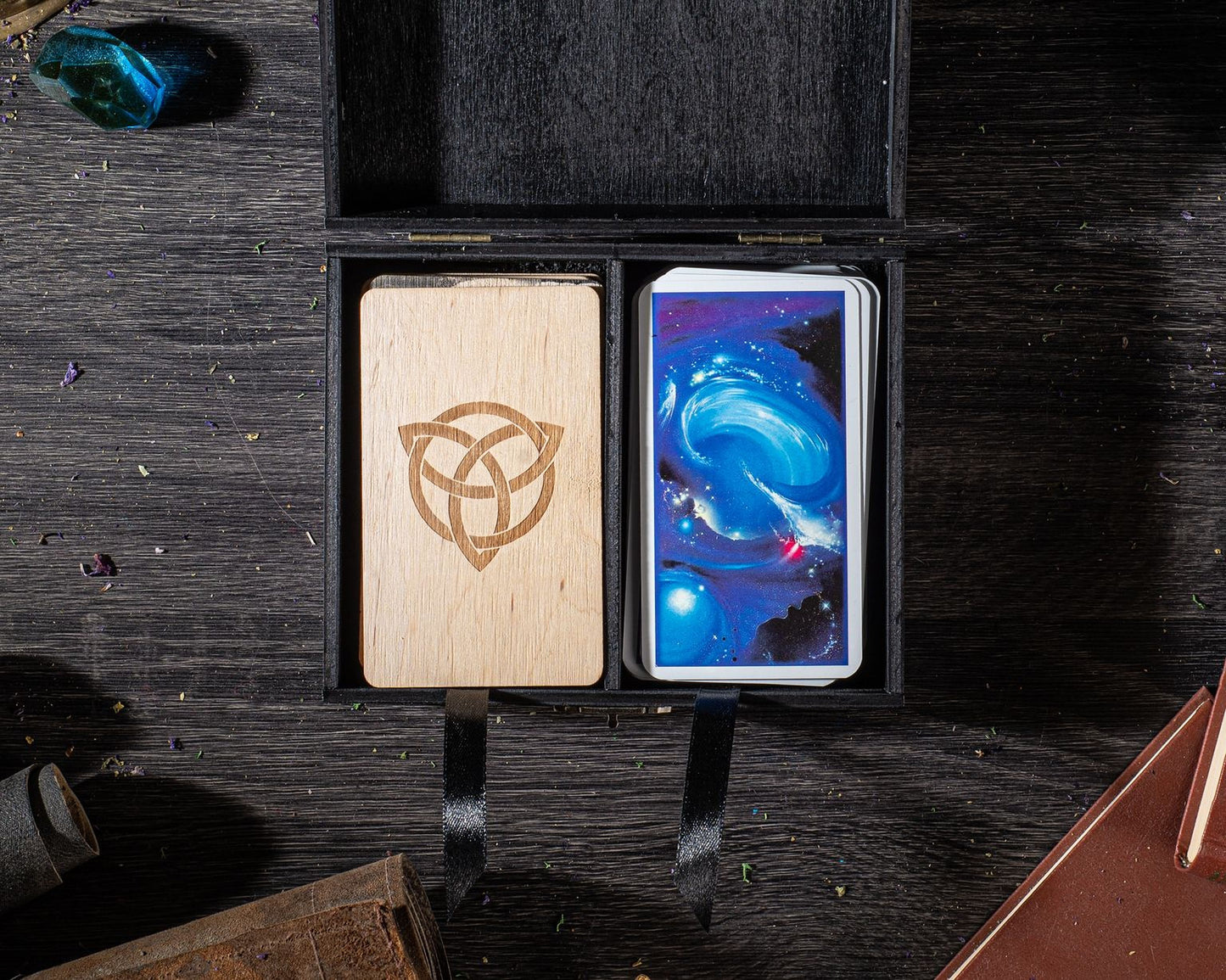 a wooden box with a crescent moon symbol on it, and a deck of playing cards inside the box, placed on a wooden surface.
