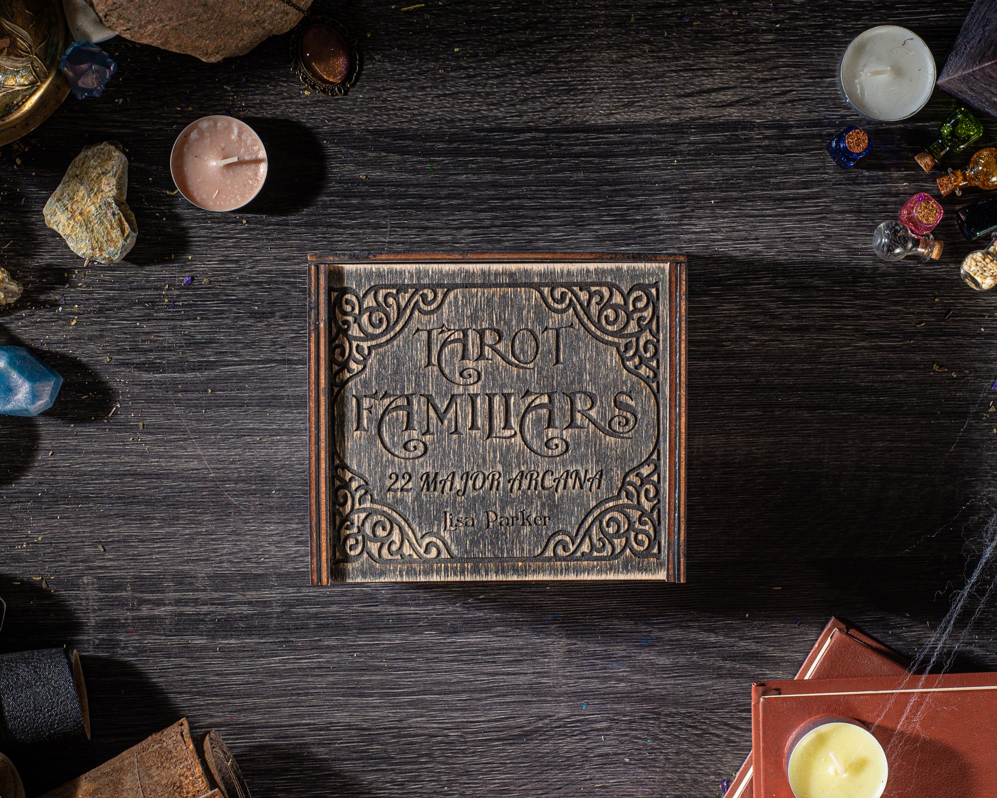 a wooden box with a decorative design, surrounded by various objects such as candles, crystals, and books on a dark wooden surface.