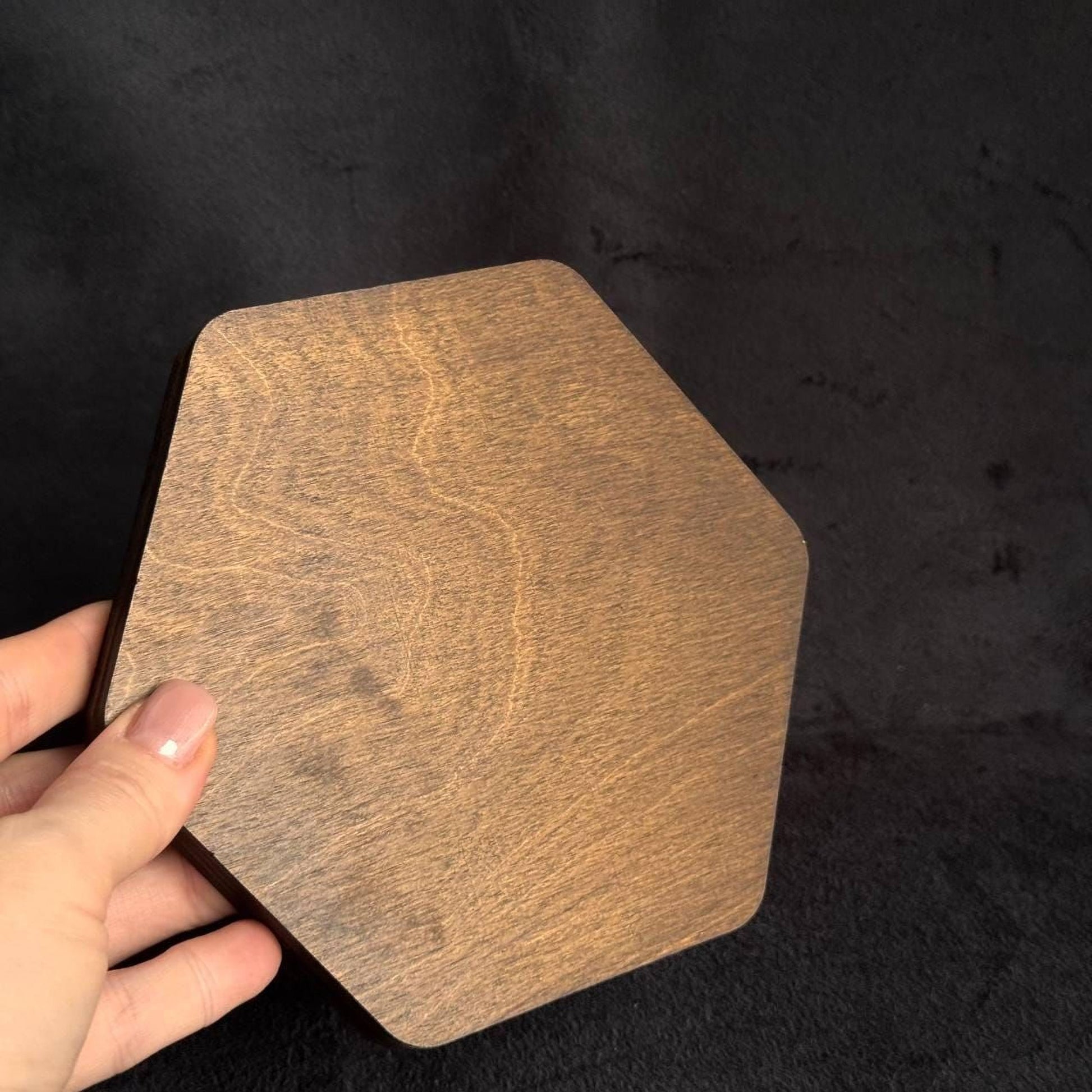 A hand is holding a wooden hexagonal object against a dark background.