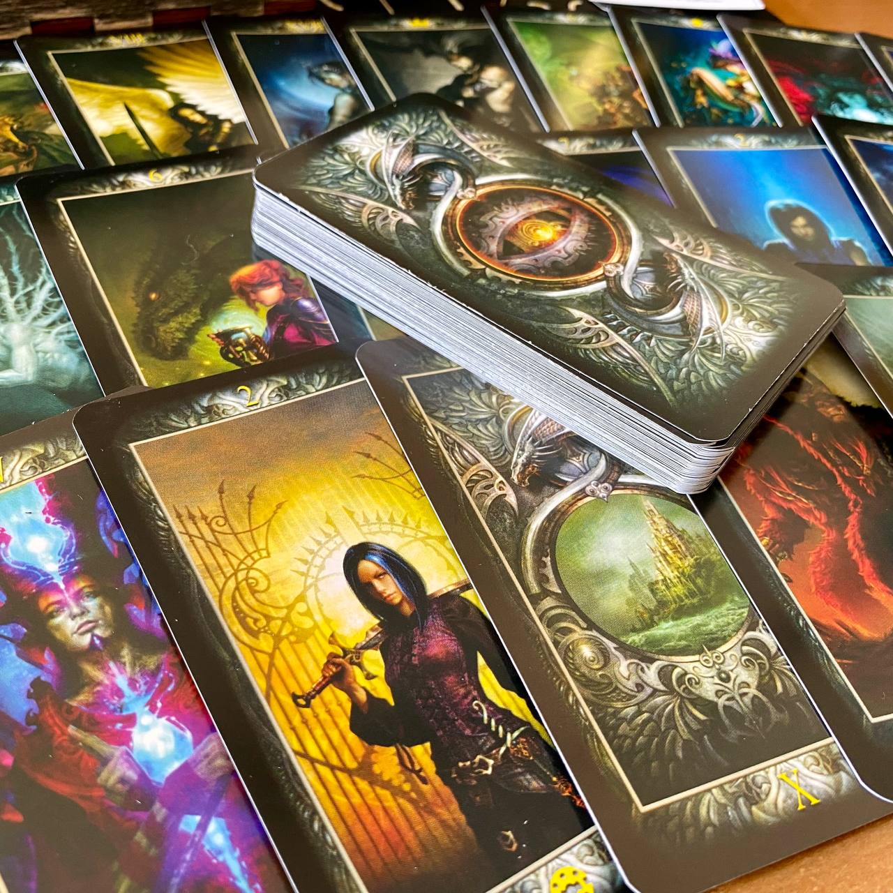 a collection of fantasy-themed tarot cards, each featuring intricate designs and vibrant colors. The cards are spread out on a surface, with some cards stacked on top of each other.